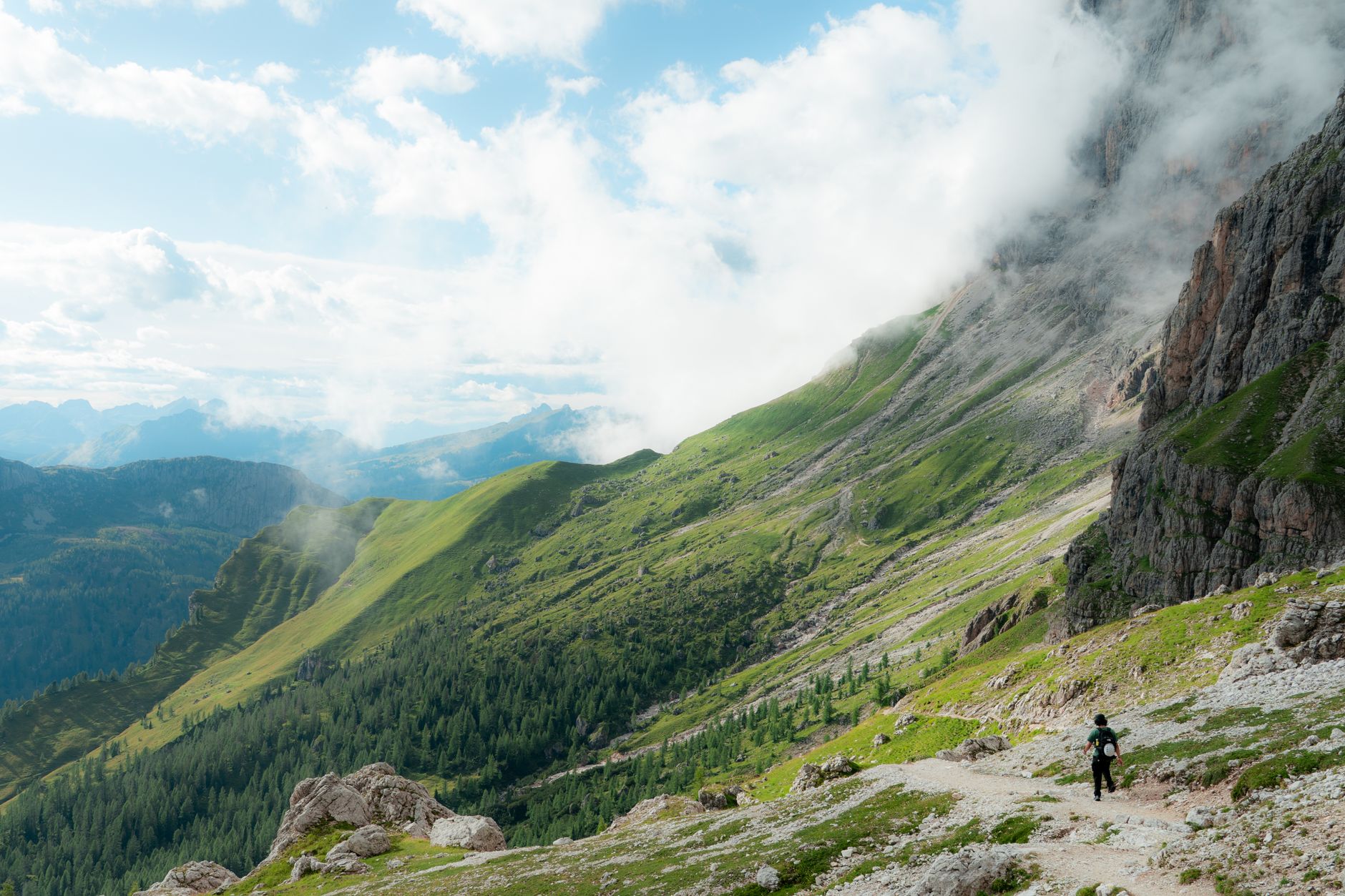 A hiker explores the lush trails of the Dolomite mountains surrounded by clouds.