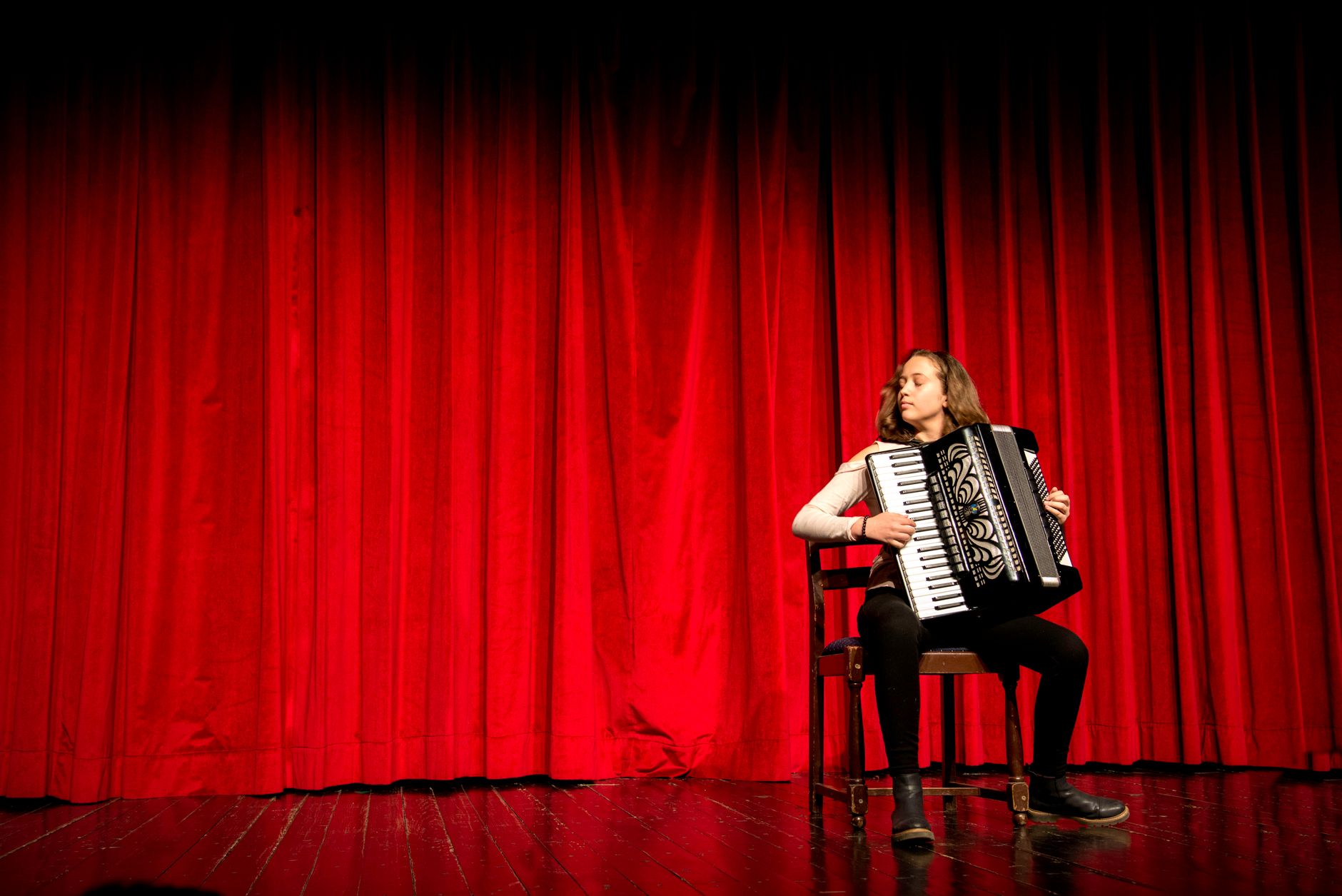 A person playing an accordion on a stage with red curtains in Novi Sad, Serbia.