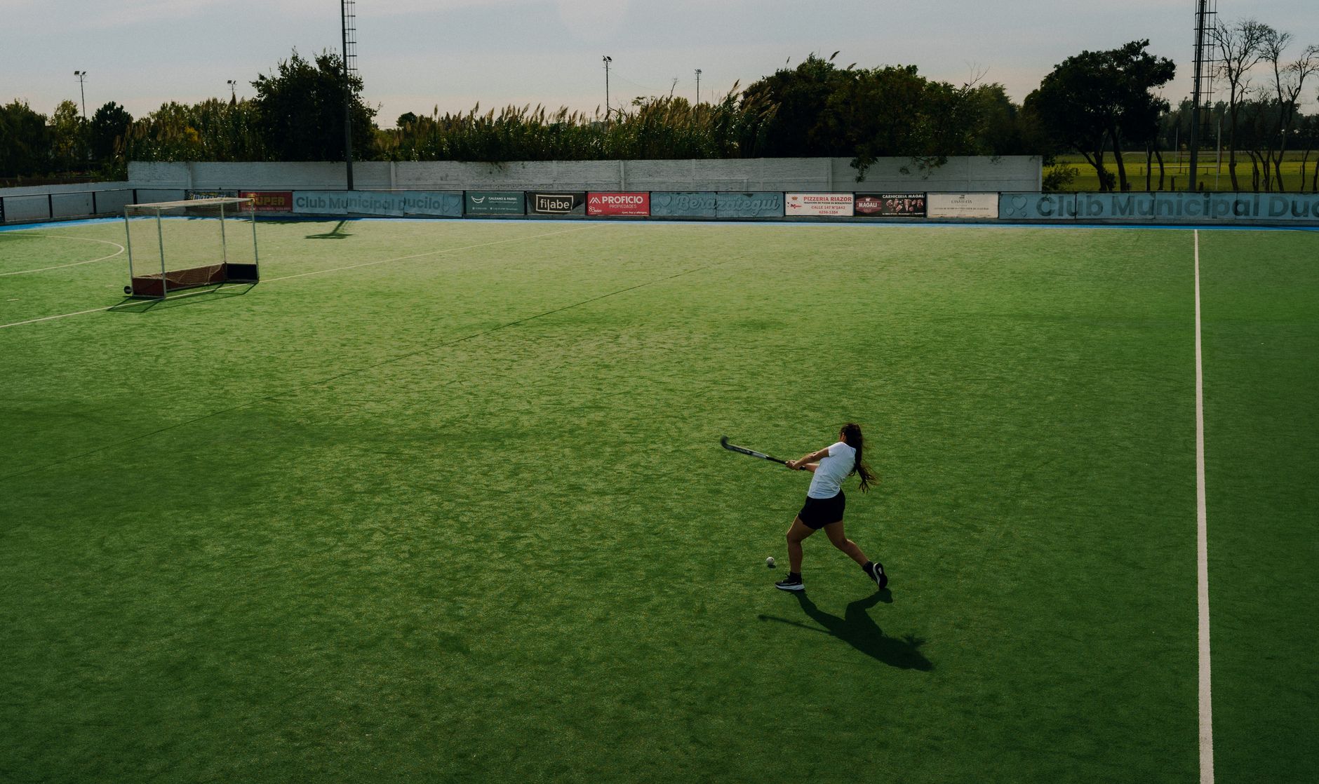A woman engaged in playing field hockey on a sunlit outdoor field.
