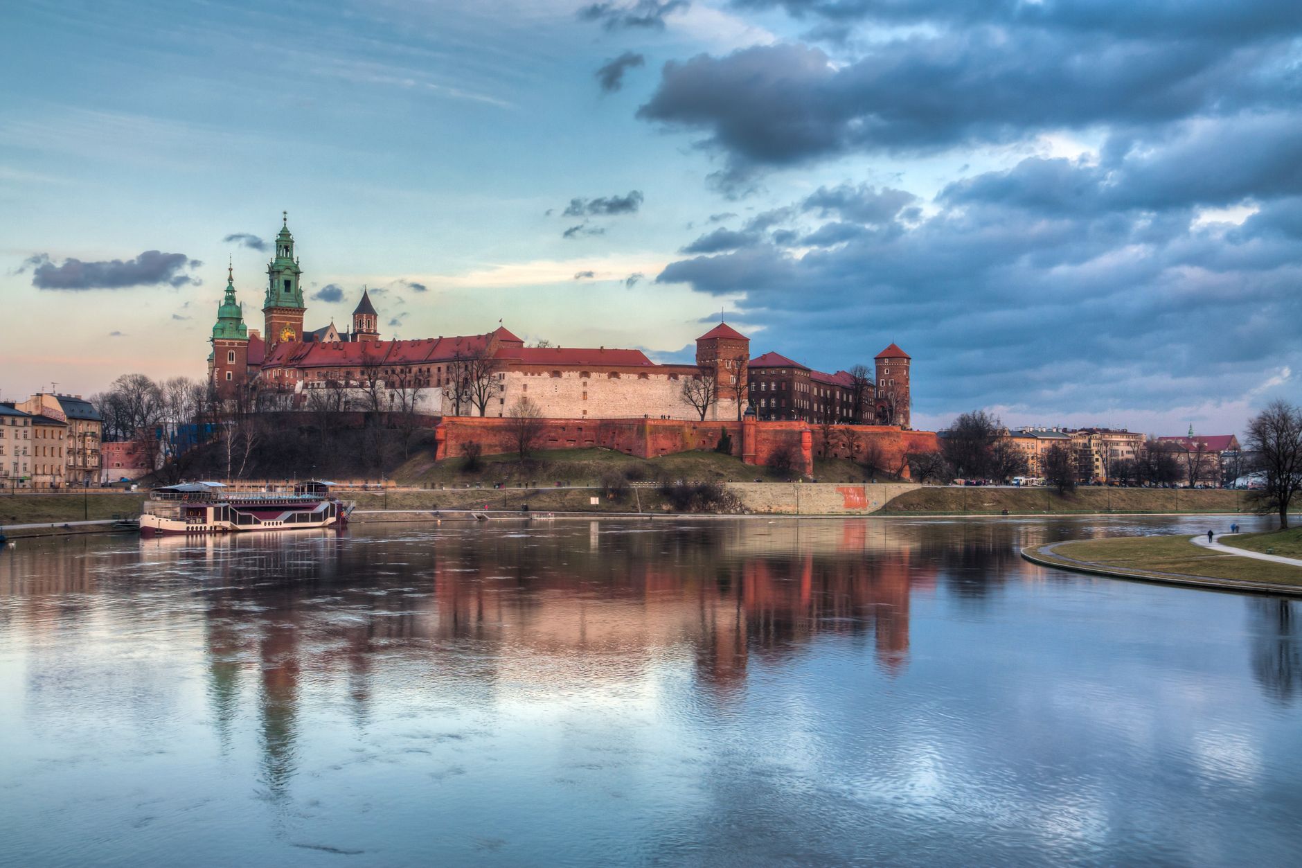 Serene view of Wawel Castle reflecting in the Vistula River at sunset in Kraków, Poland.