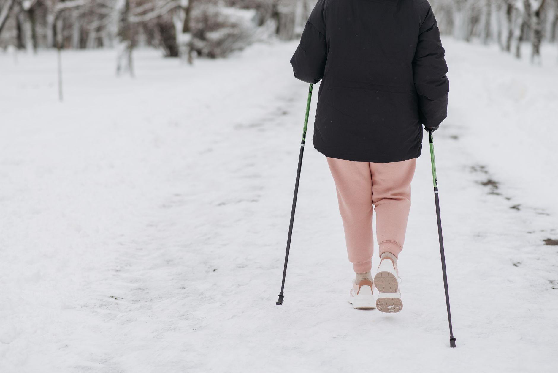 Person walking on snow-covered path with trekking poles in a winter landscape.