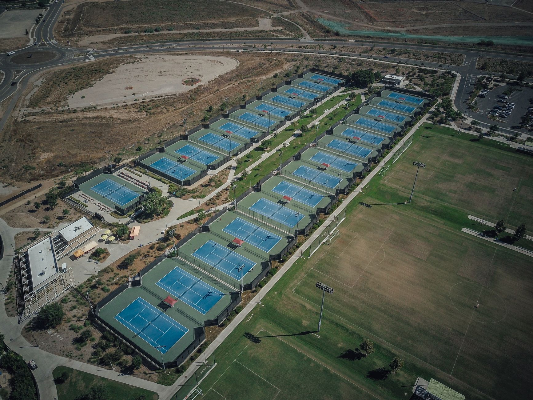High-angle view of multiple tennis courts in a landscaped area, suitable for sports activities.