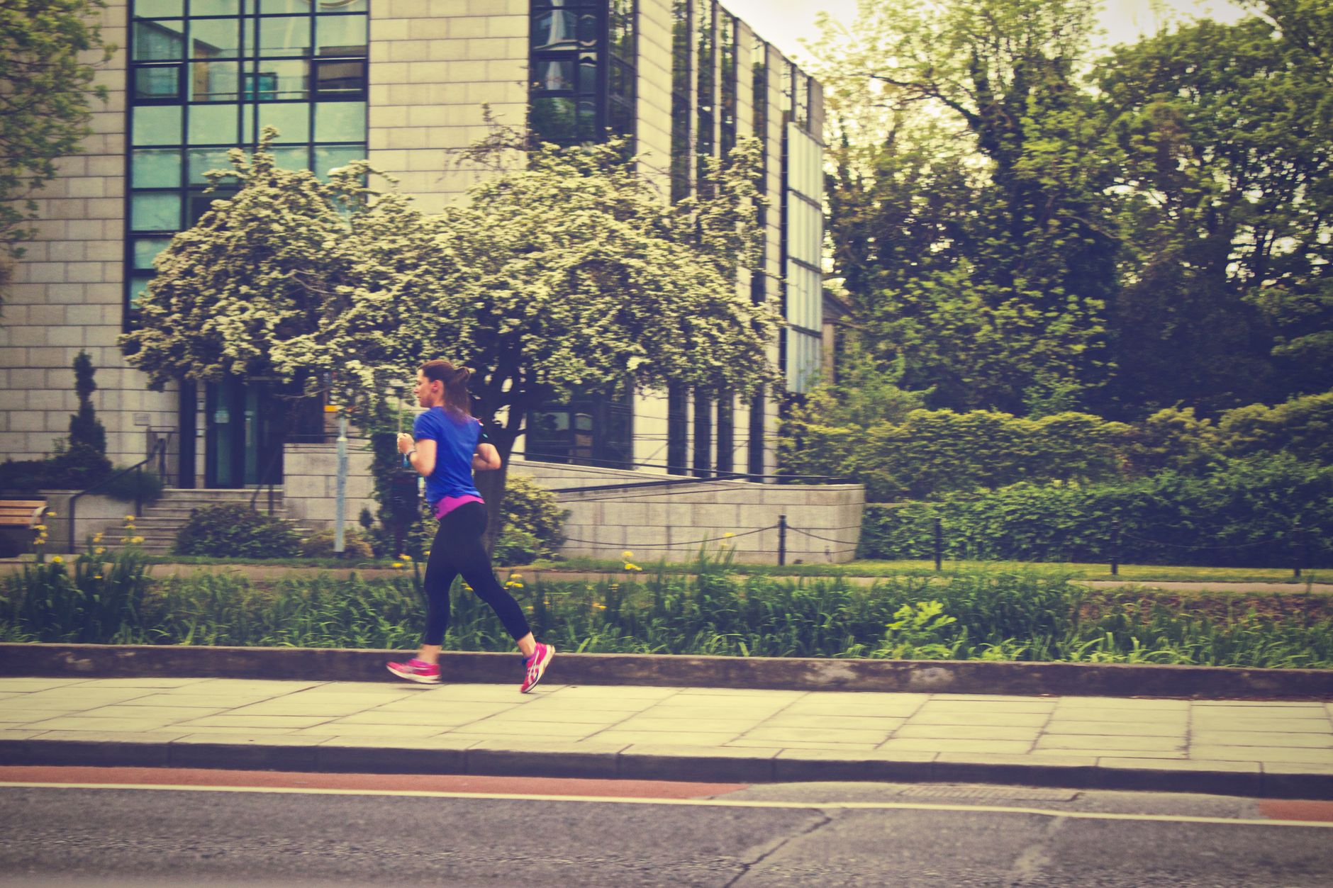 A woman running along a city street during the day surrounded by nature.