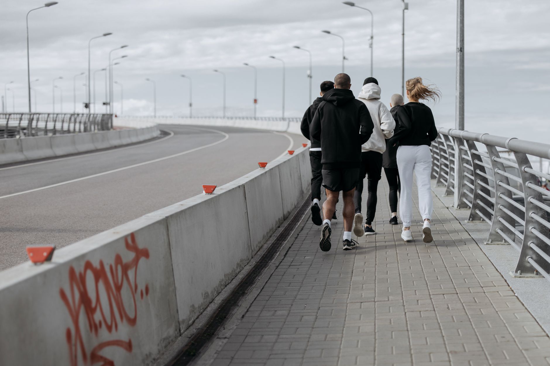 A group of people jogging on a bridge with graffiti, showcasing outdoor fitness and urban lifestyle.