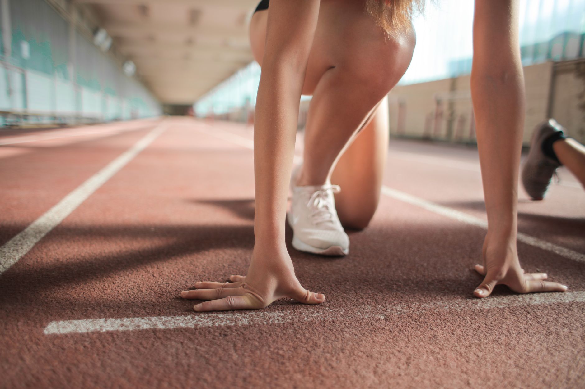 Faceless female sprinter in running crouch start pose putting hands on starting line on track
