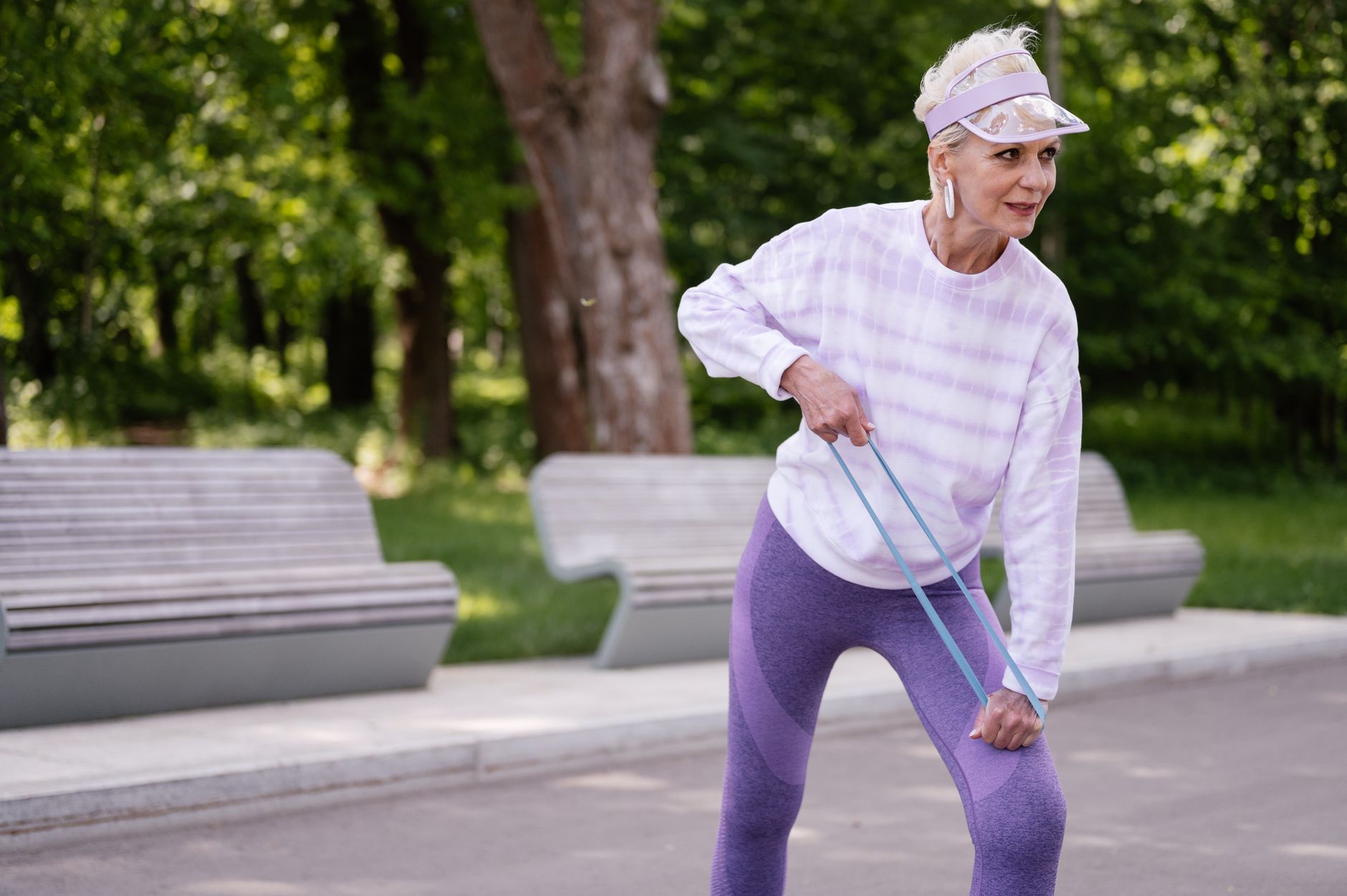 Senior woman performing outdoor exercise with a resistance band in a park setting.