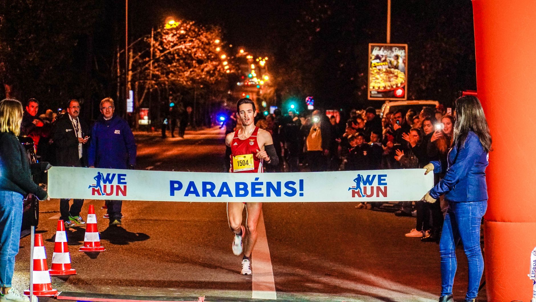 Runner crosses finish line in nighttime marathon, celebrating victory.