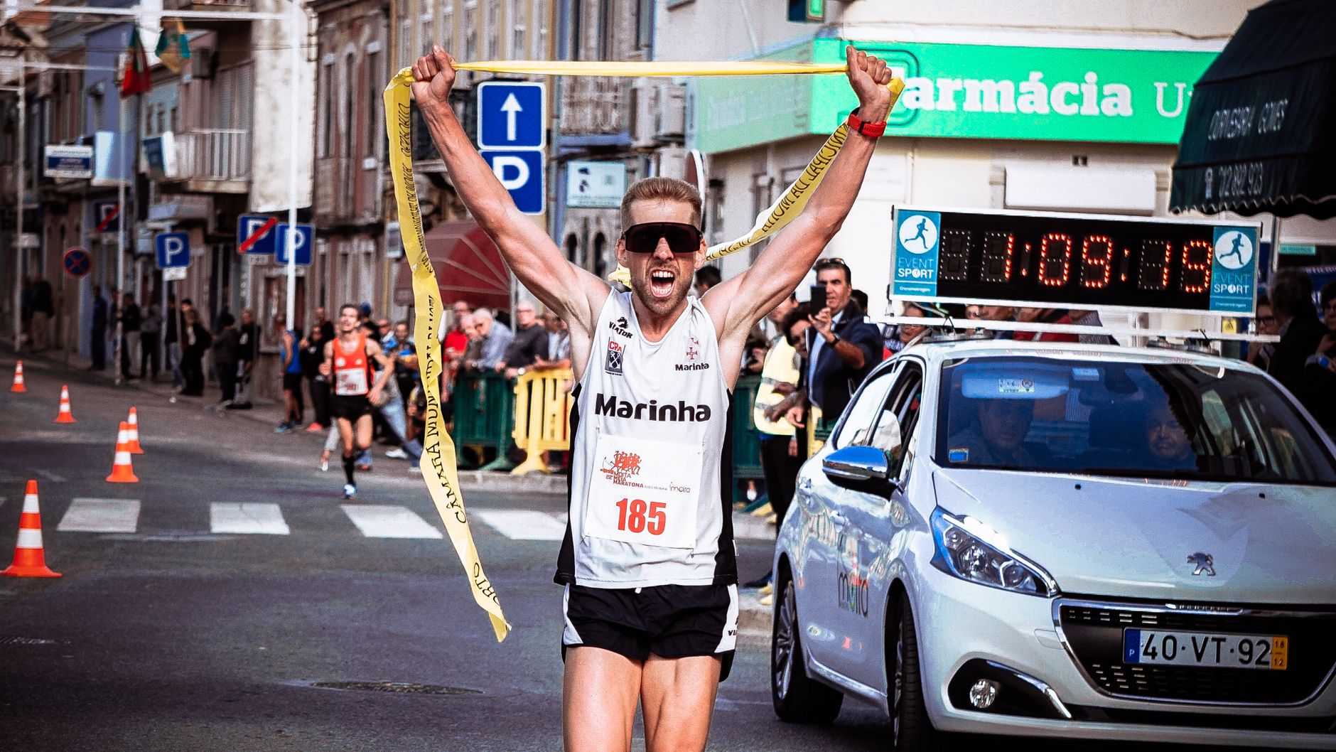 A marathon runner triumphantly crosses the finish line in an urban race setting, celebrated by onlookers.