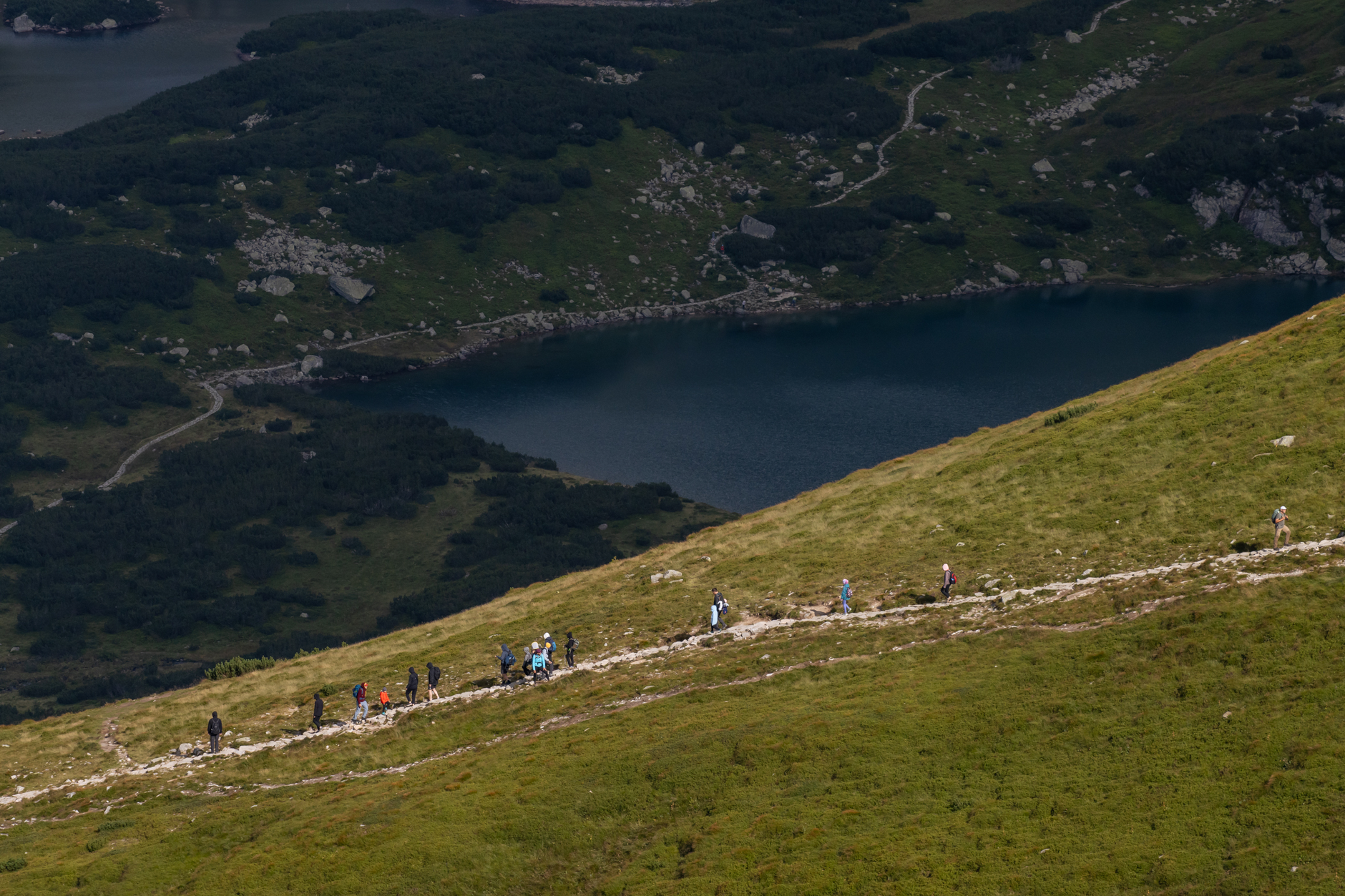 Hikers explore a picturesque trail in Zakopane, Poland, with breathtaking mountain views and a serene lake.