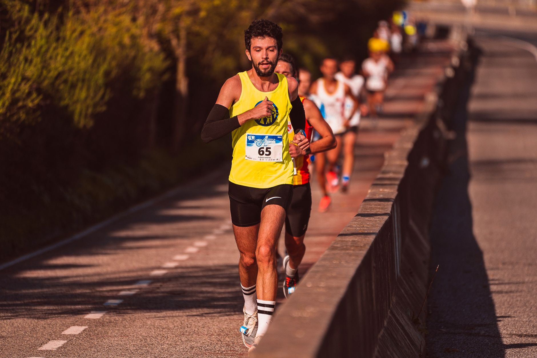 Focused male athlete running in a marathon on a sunlit road, leading a group of runners.