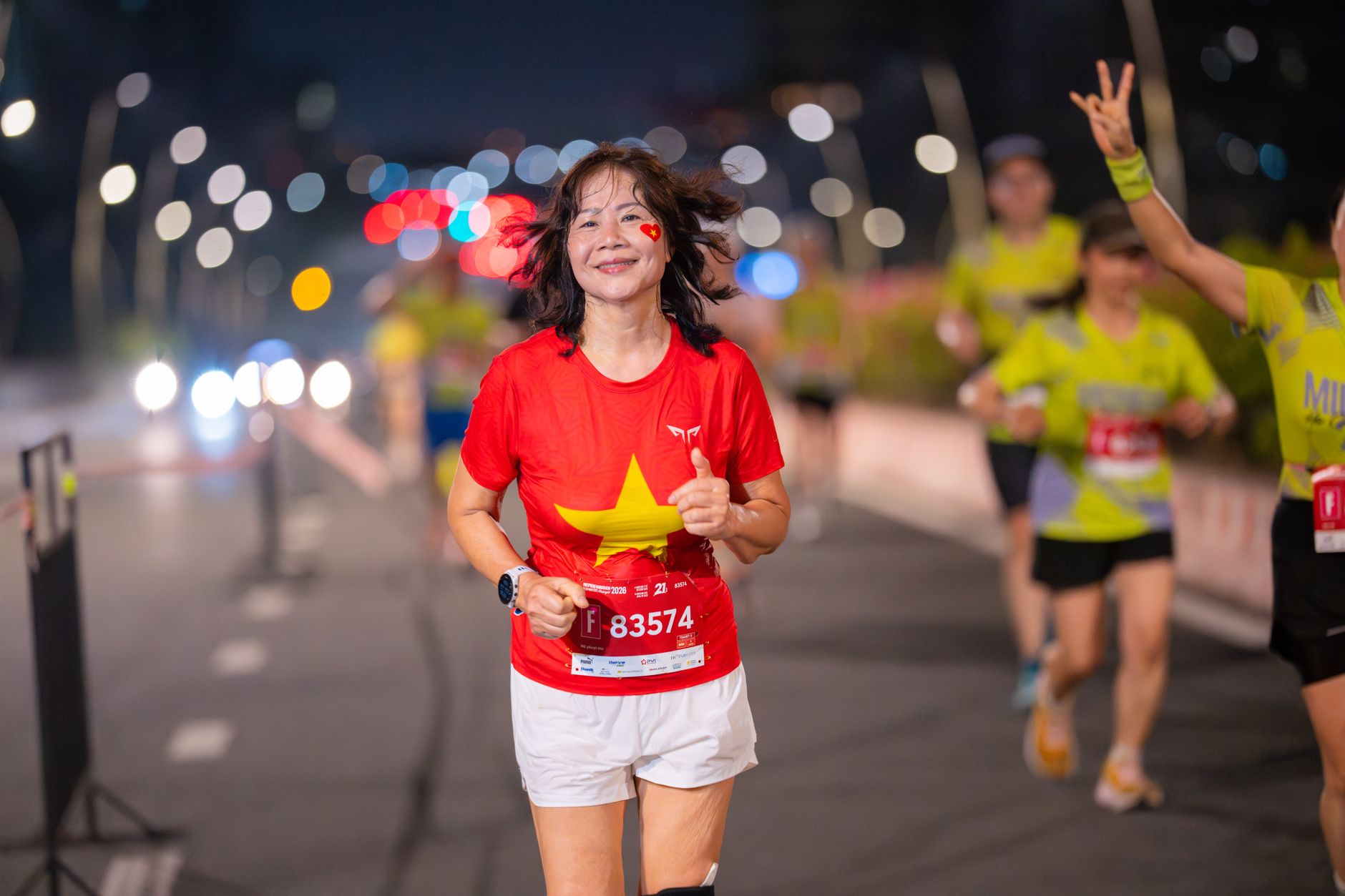 A female marathon runner with a joyful smile under city lights during a nighttime race.