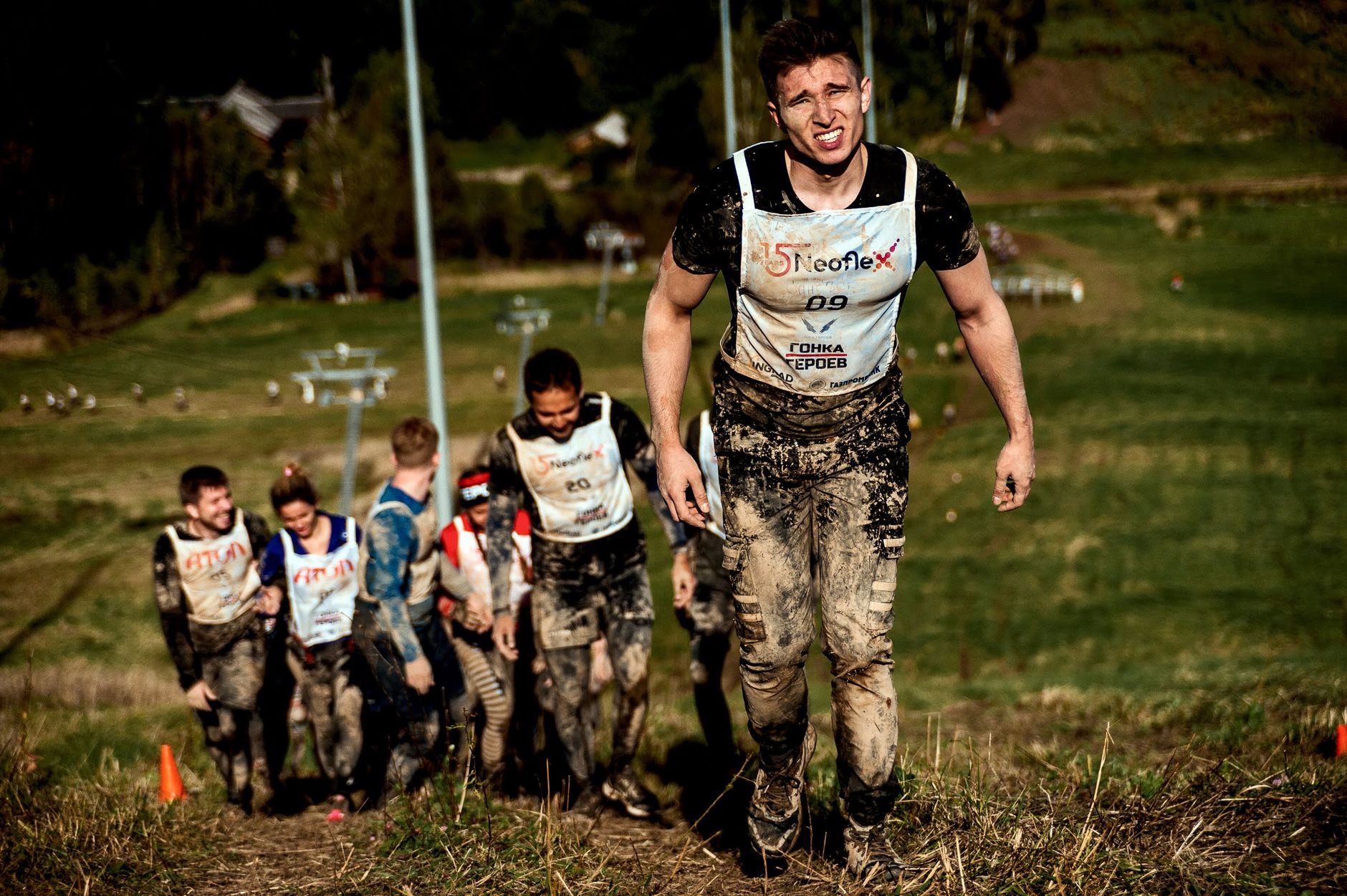Group of determined competitors battling a muddy hill during an outdoor obstacle race.