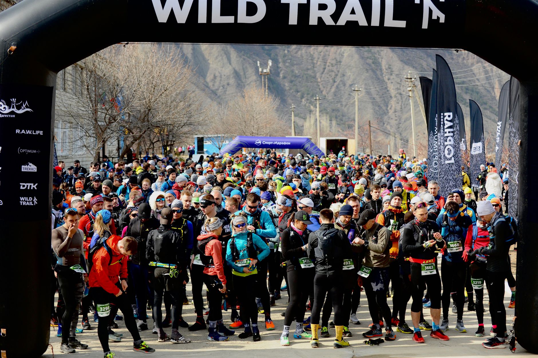 A large group of runners prepares for an exciting outdoor marathon race under a Wild Trail arch.