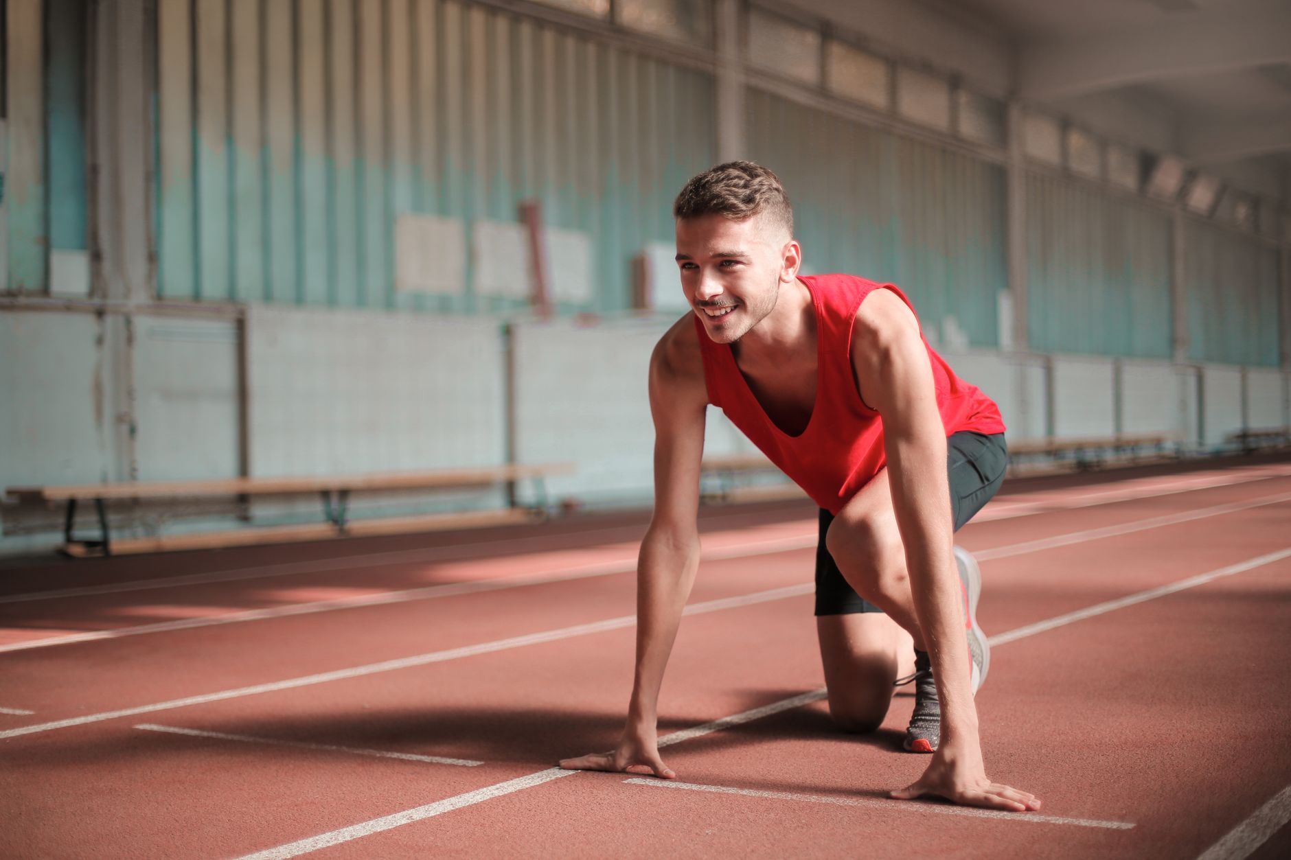 A young male athlete preparing to start running on an indoor track with a smile.