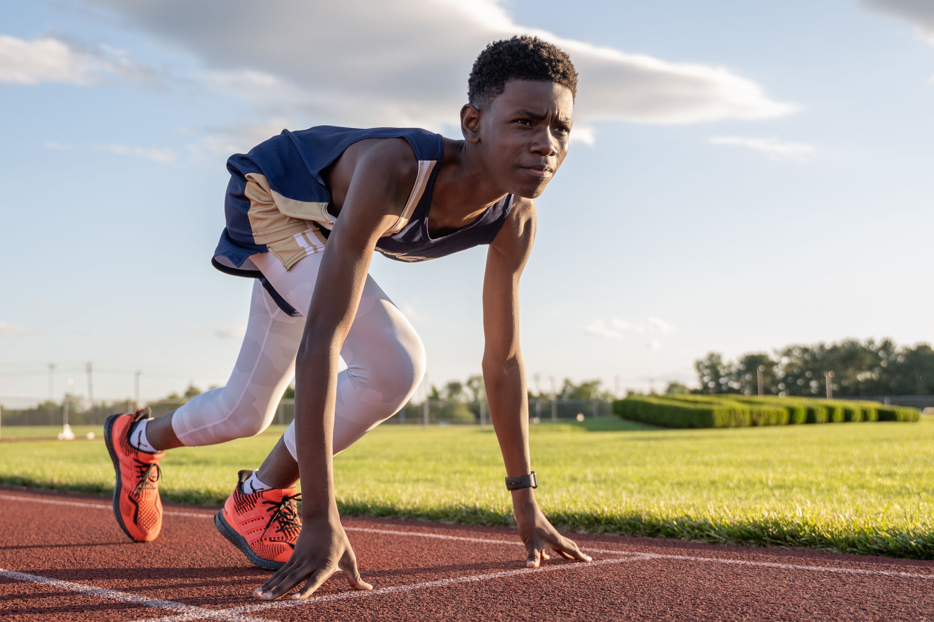 Focused young athlete in starting position on sunny outdoor track ready to sprint.