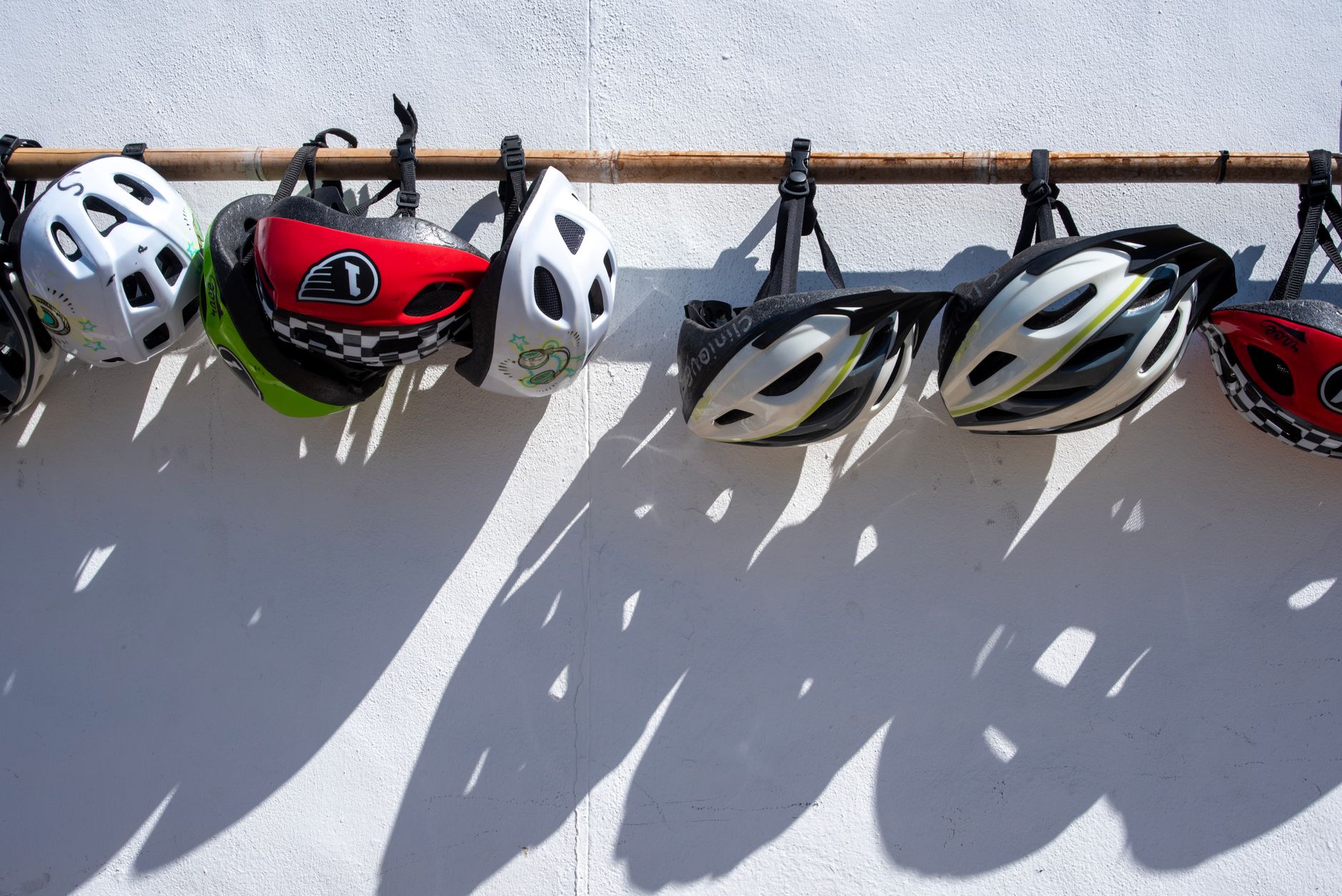 A row of colorful bike helmets hanging on a wall, casting shadows.