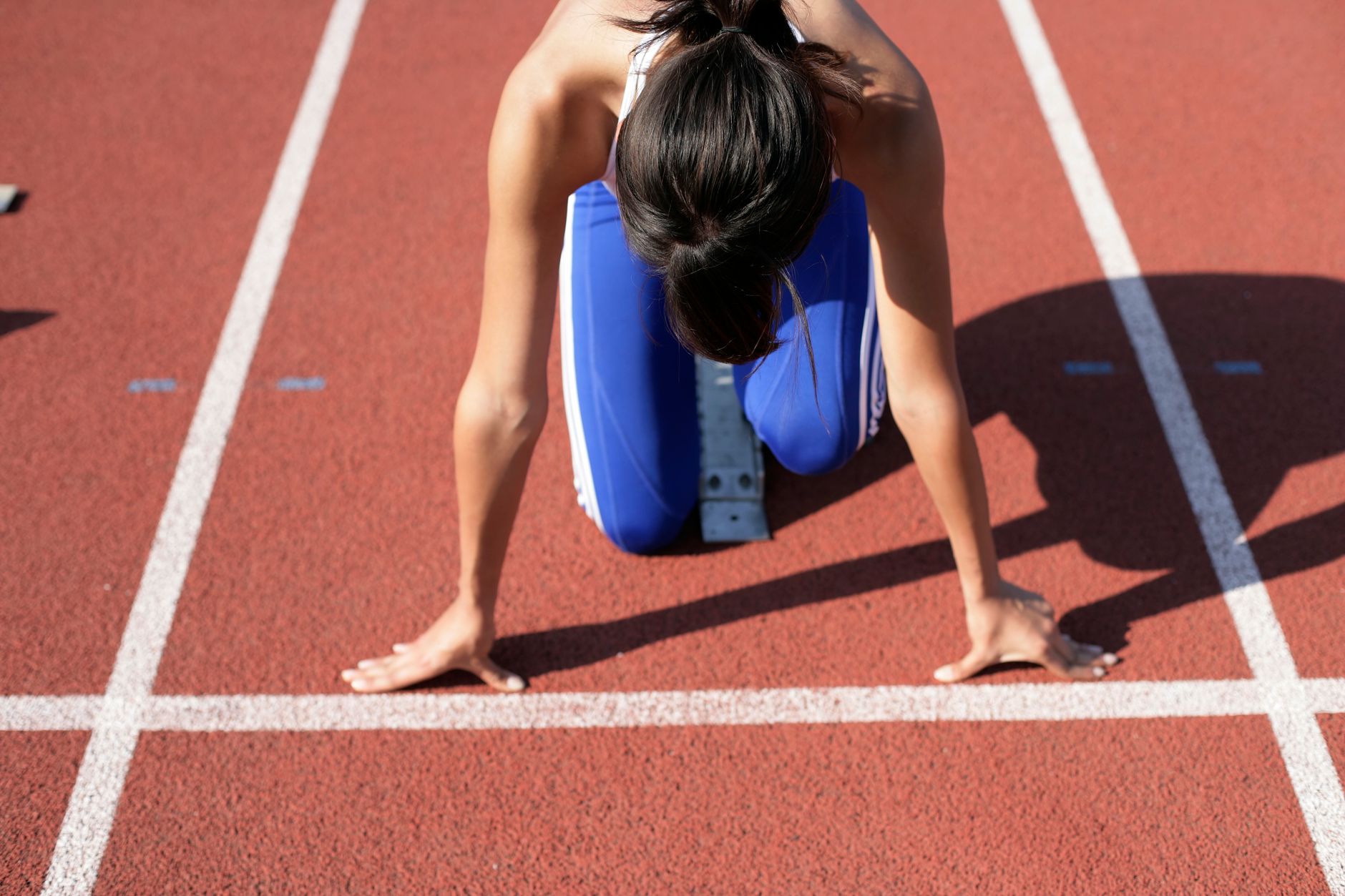 A female athlete crouches at the starting line, ready to sprint on a sunny day.