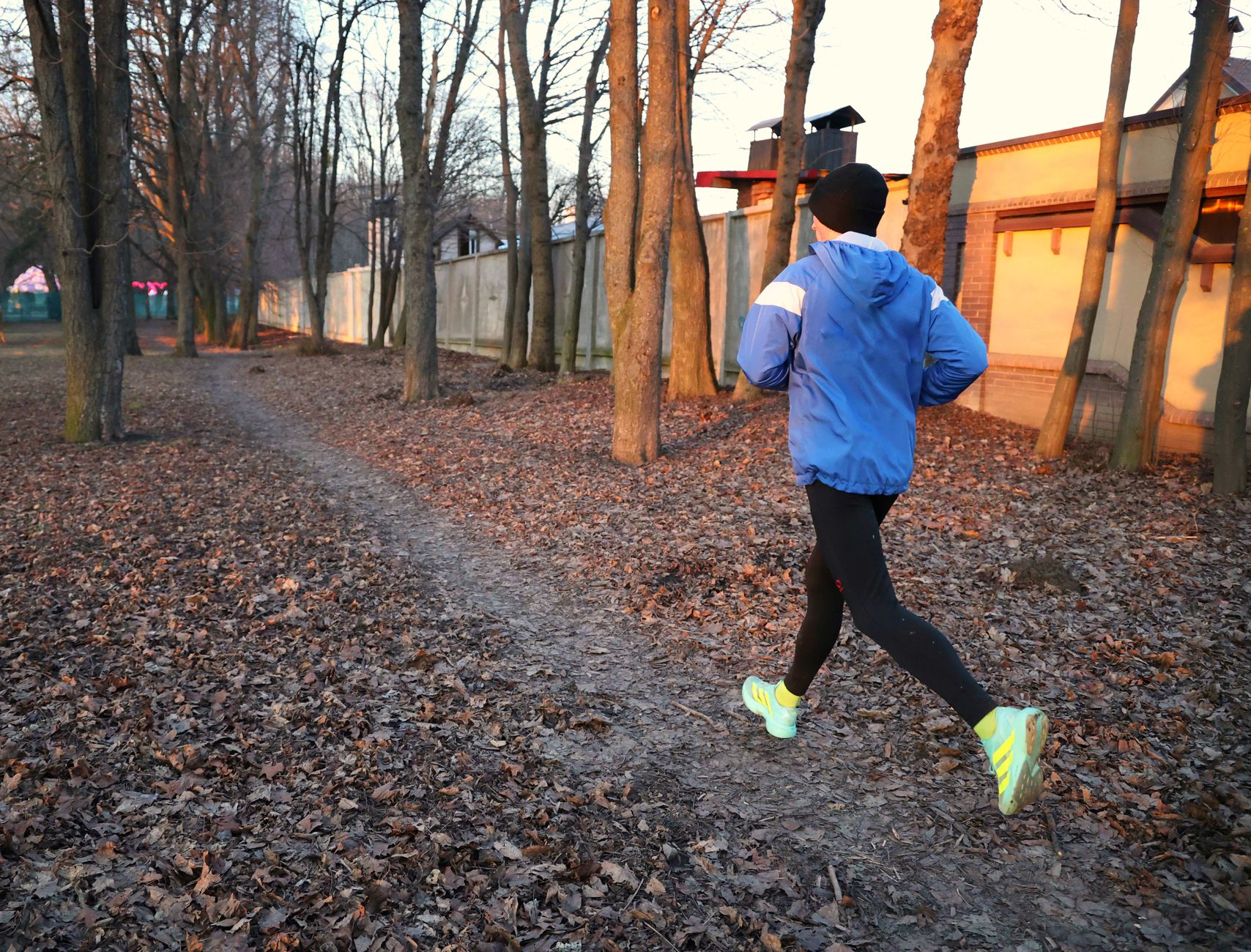 A person runs along a leaf-strewn path in an autumn park, wearing bright athletic gear.