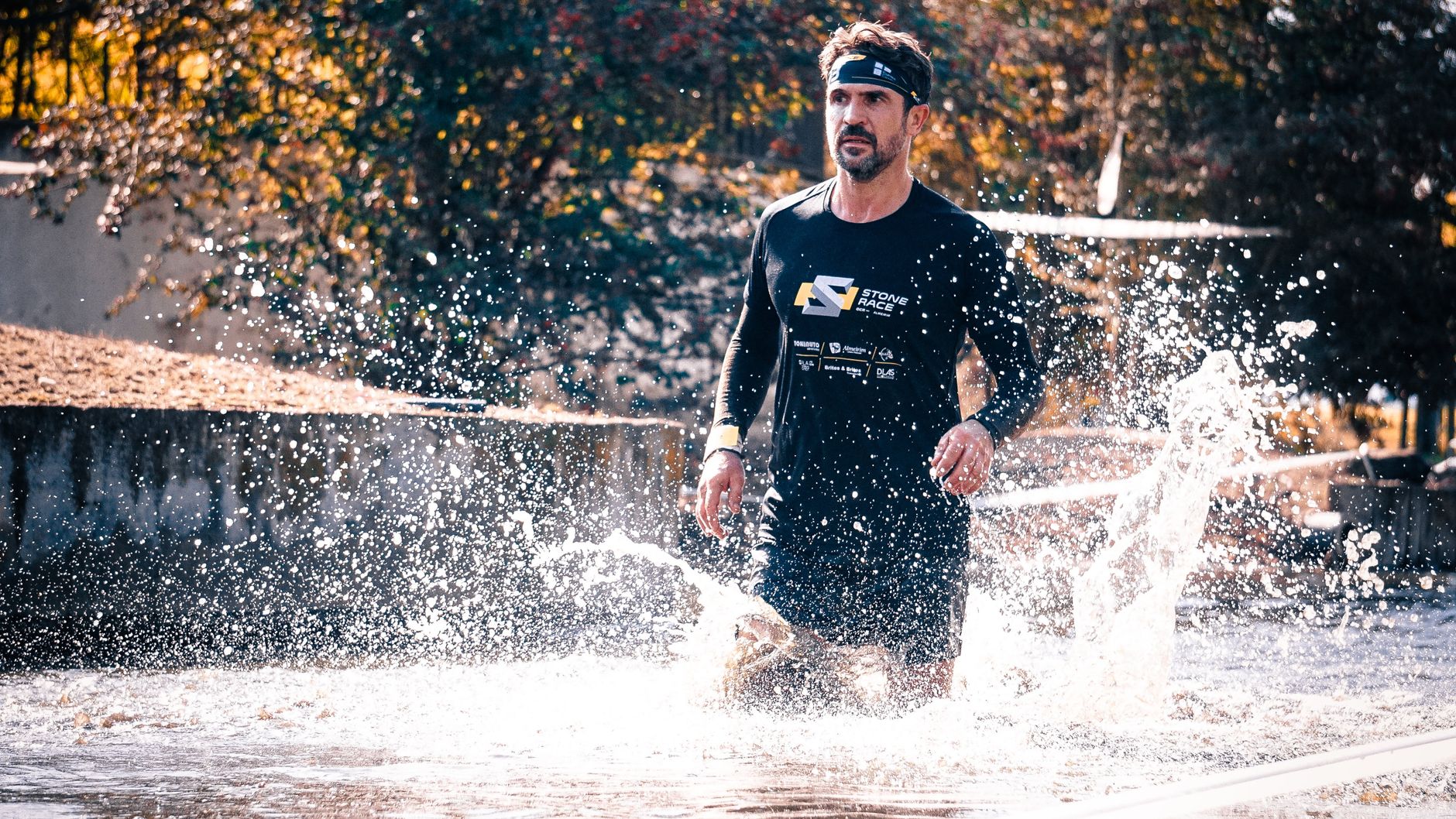 Athlete running through water splash during outdoor obstacle race.