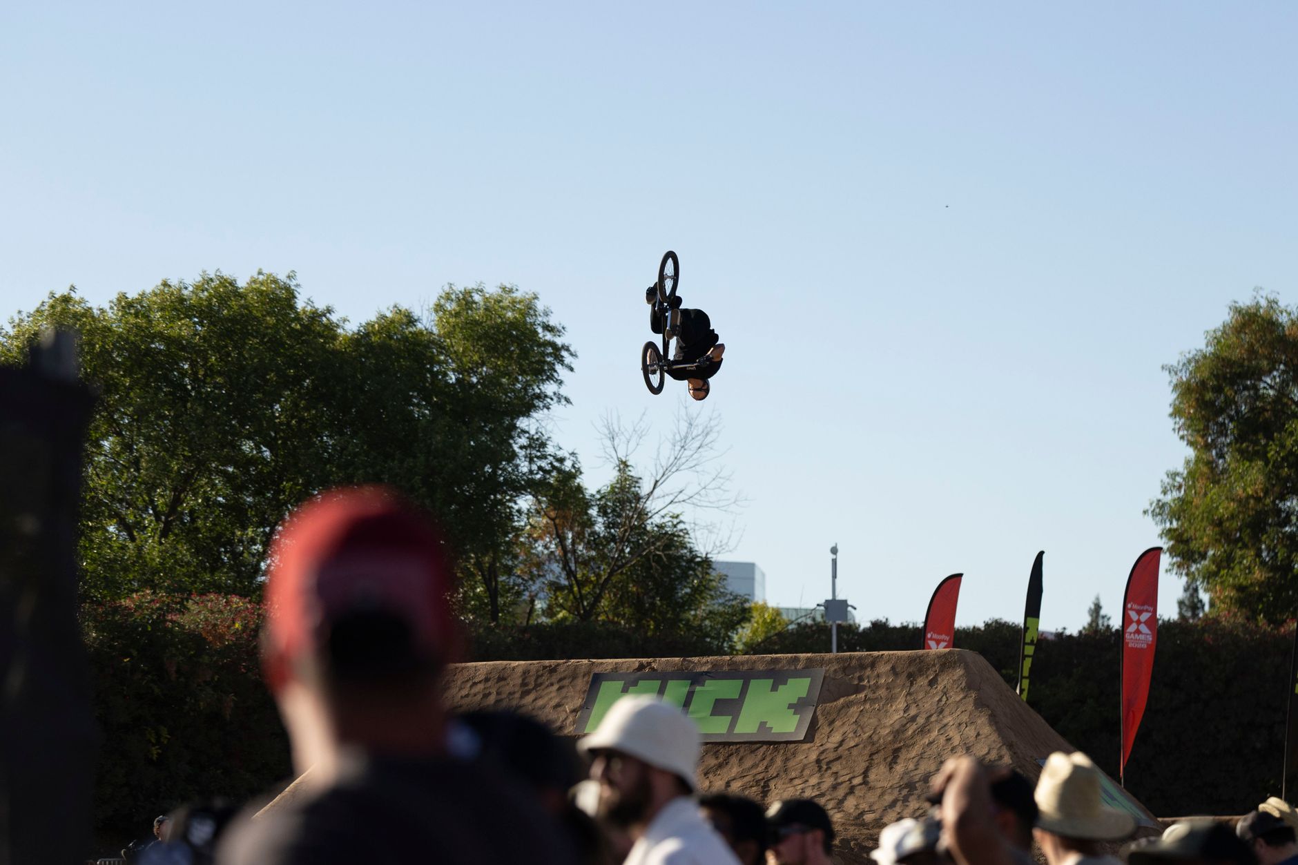 BMX rider executes an impressive aerial trick against a clear blue sky during an outdoor event.