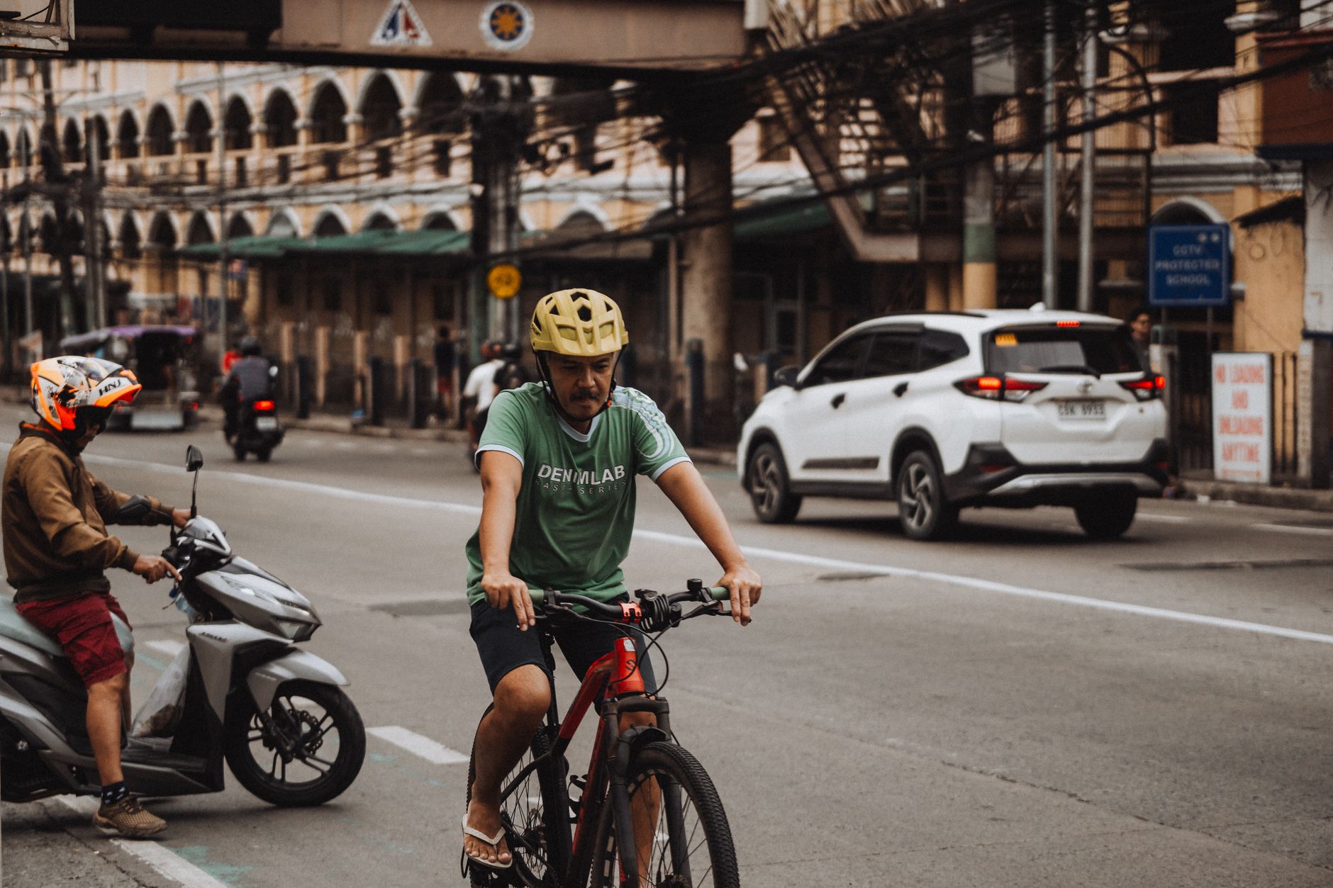A cyclist wearing a helmet rides alongside city traffic in a bustling urban area street.