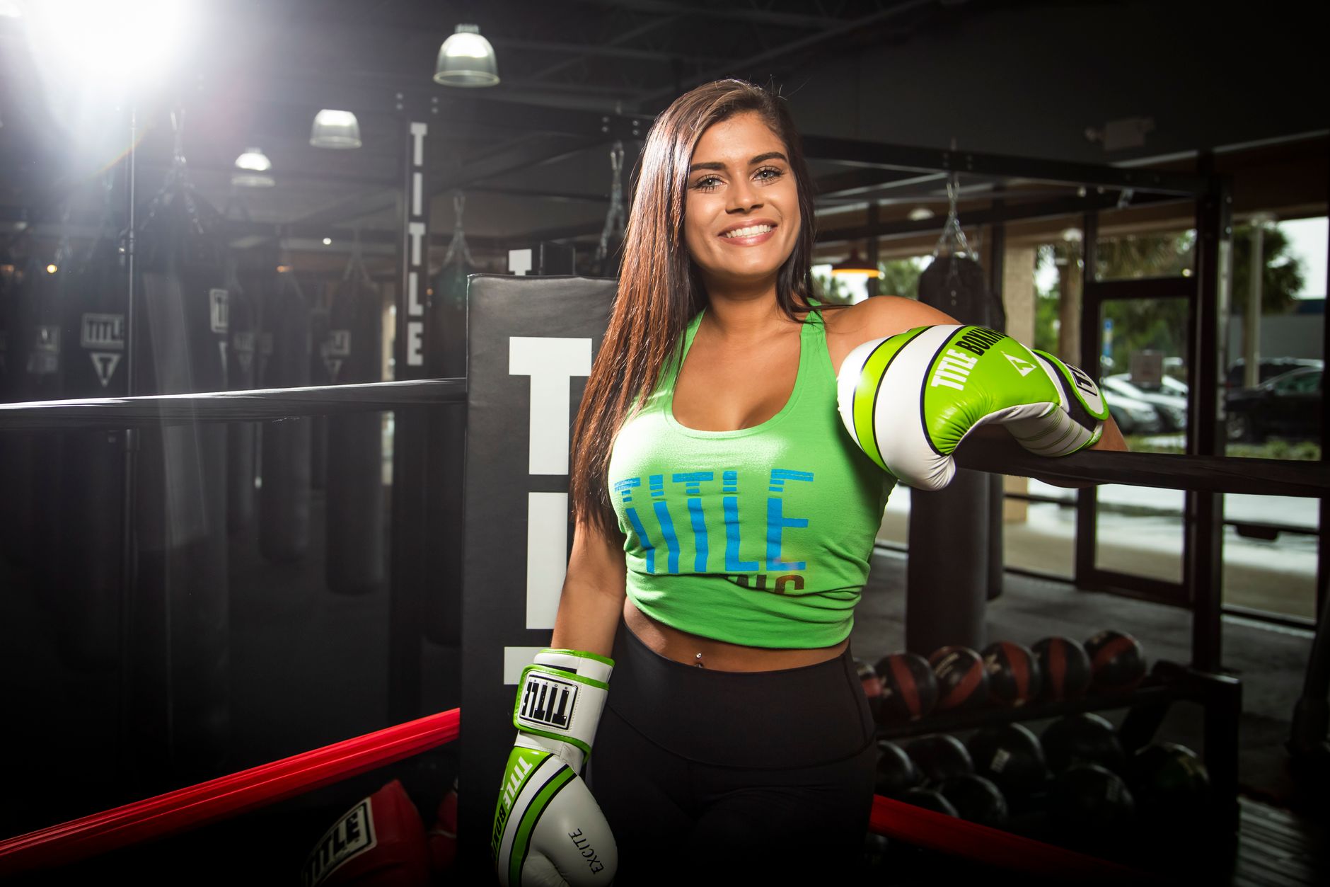 Confident female boxer in a gym wearing green gloves, posing inside the boxing ring.