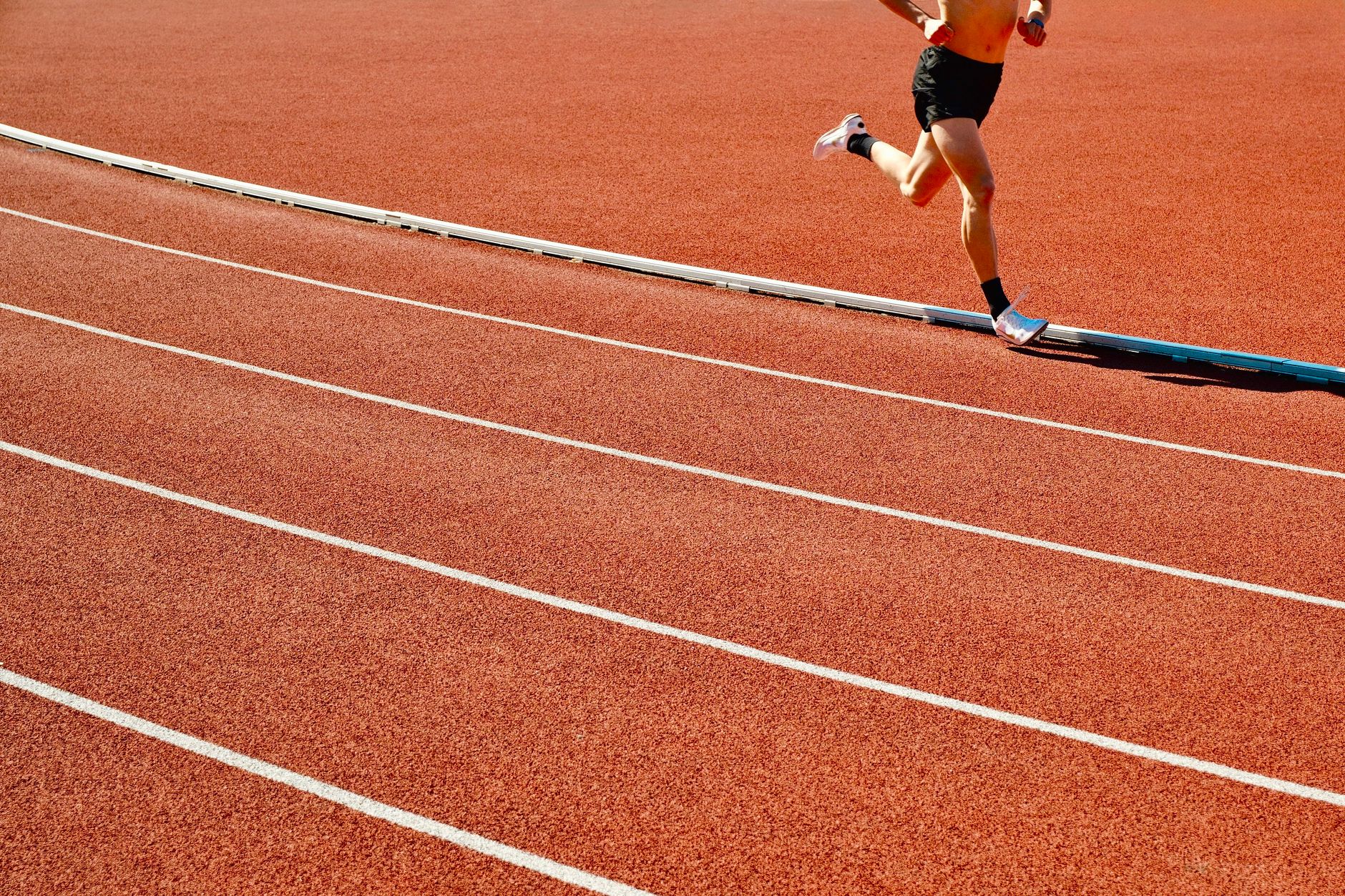 Athlete running on a red track in an outdoor stadium on a sunny day.