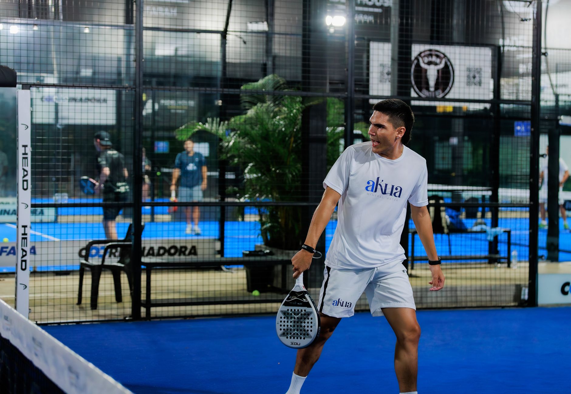 Energetic padel tennis player at indoor court mid-match.