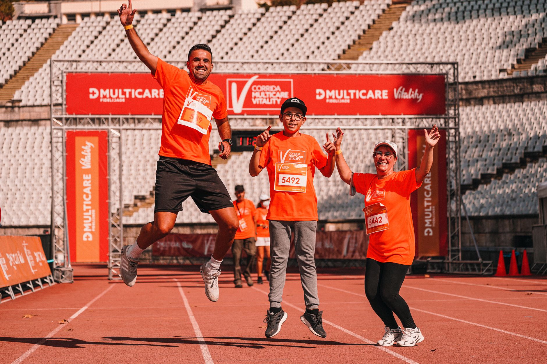 Cheerful family jumping for joy at the finish line of an outdoor race, wearing matching orange shirts.