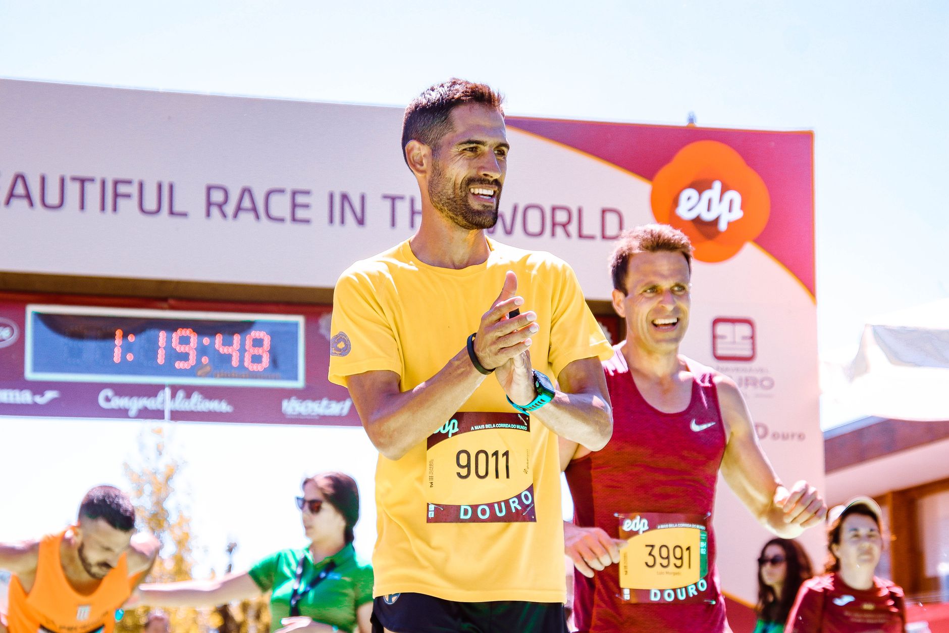 Marathon runners celebrating their successful finish at a race event in bright daylight.