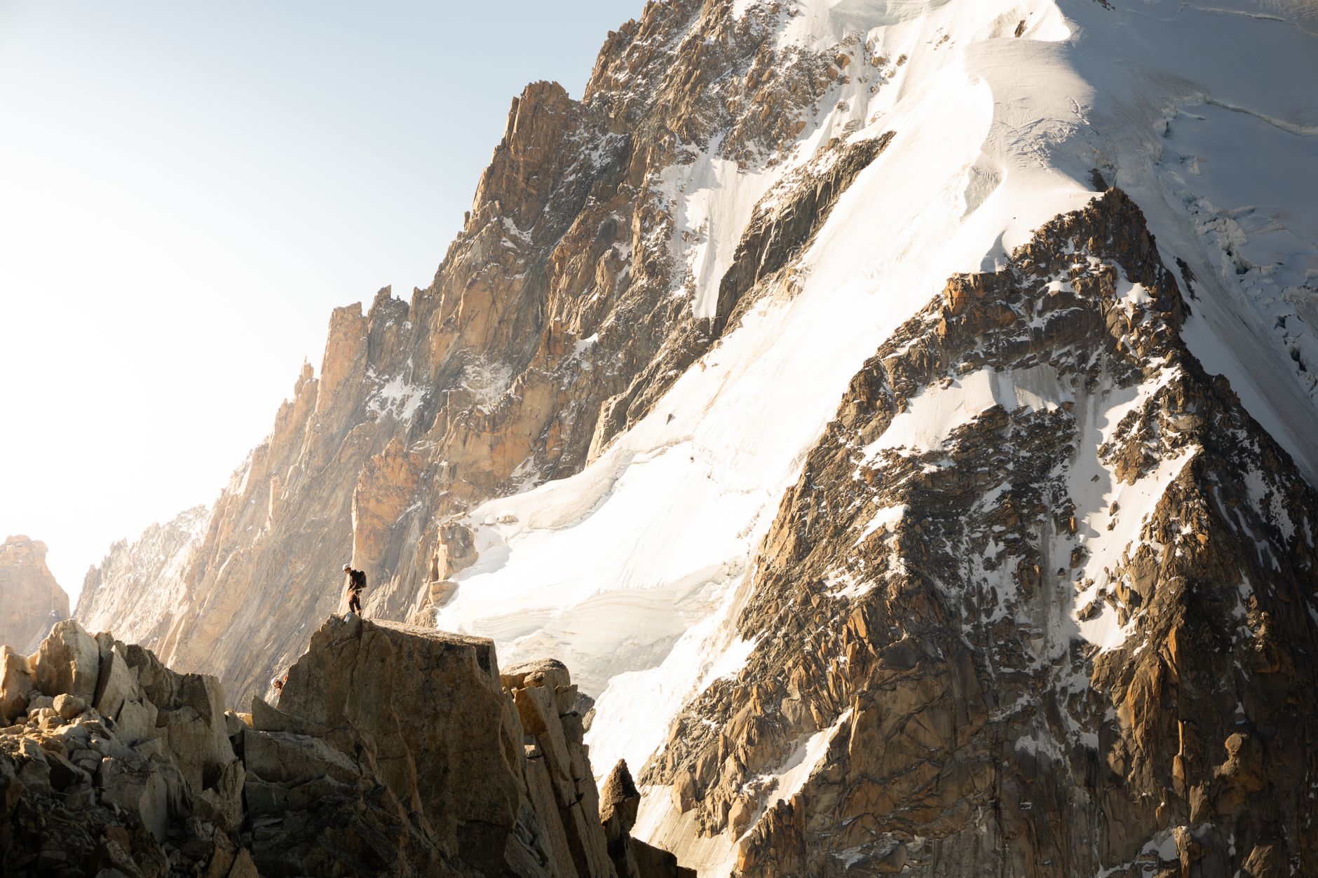 Dramatic scene of a mountaineer scaling the rugged peaks of Chamonix in midday sun.