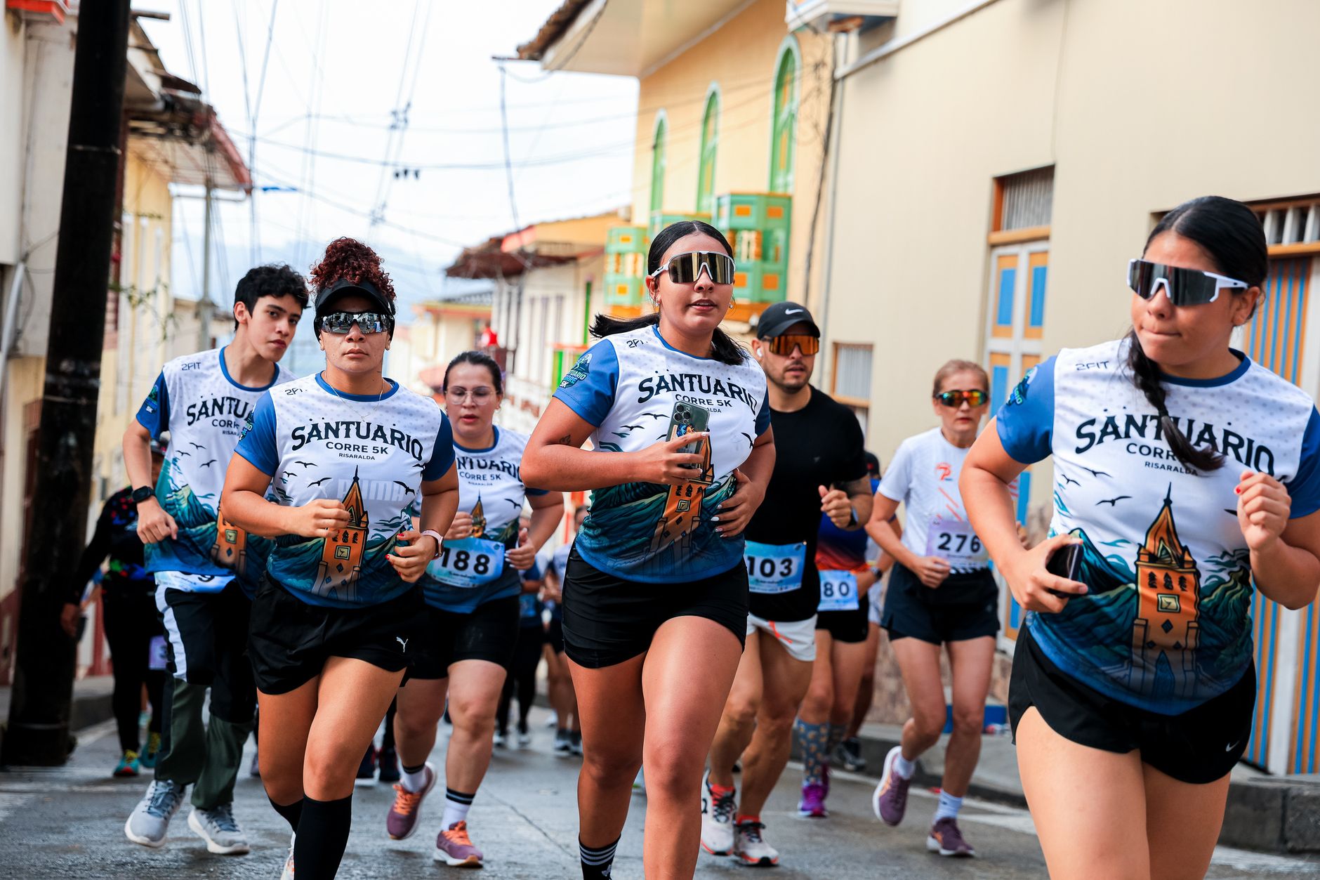 Participants in a vibrant street race wearing athletic wear and numbered bibs, running energetically.