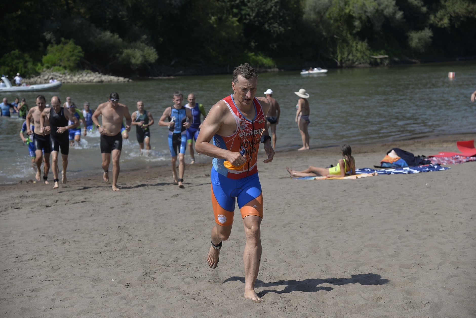 Action shot of triathletes transitioning from swim to run along Jánd riverbank.