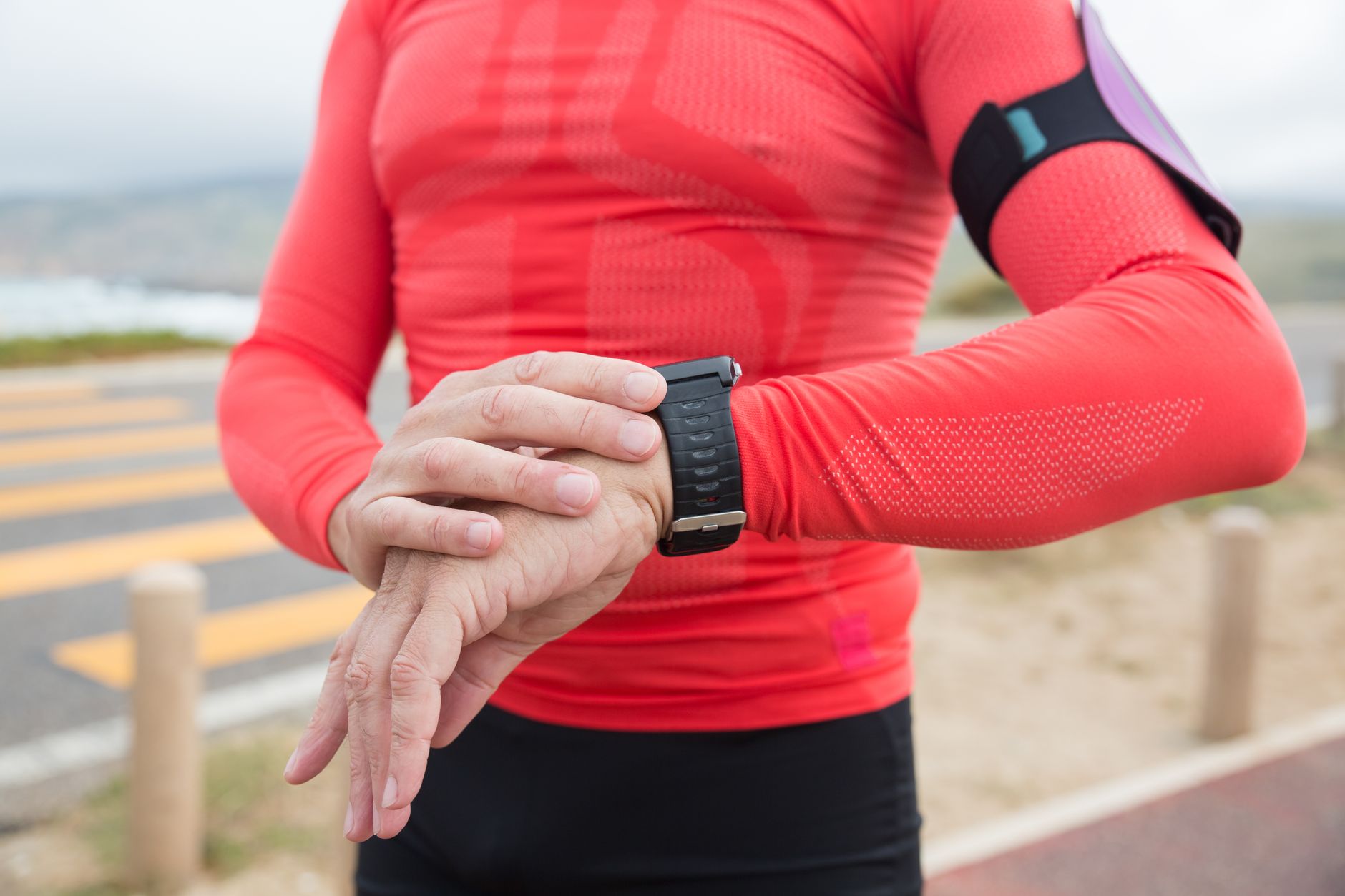 A person in red activewear checks their wristwatch during an outdoor exercise session.