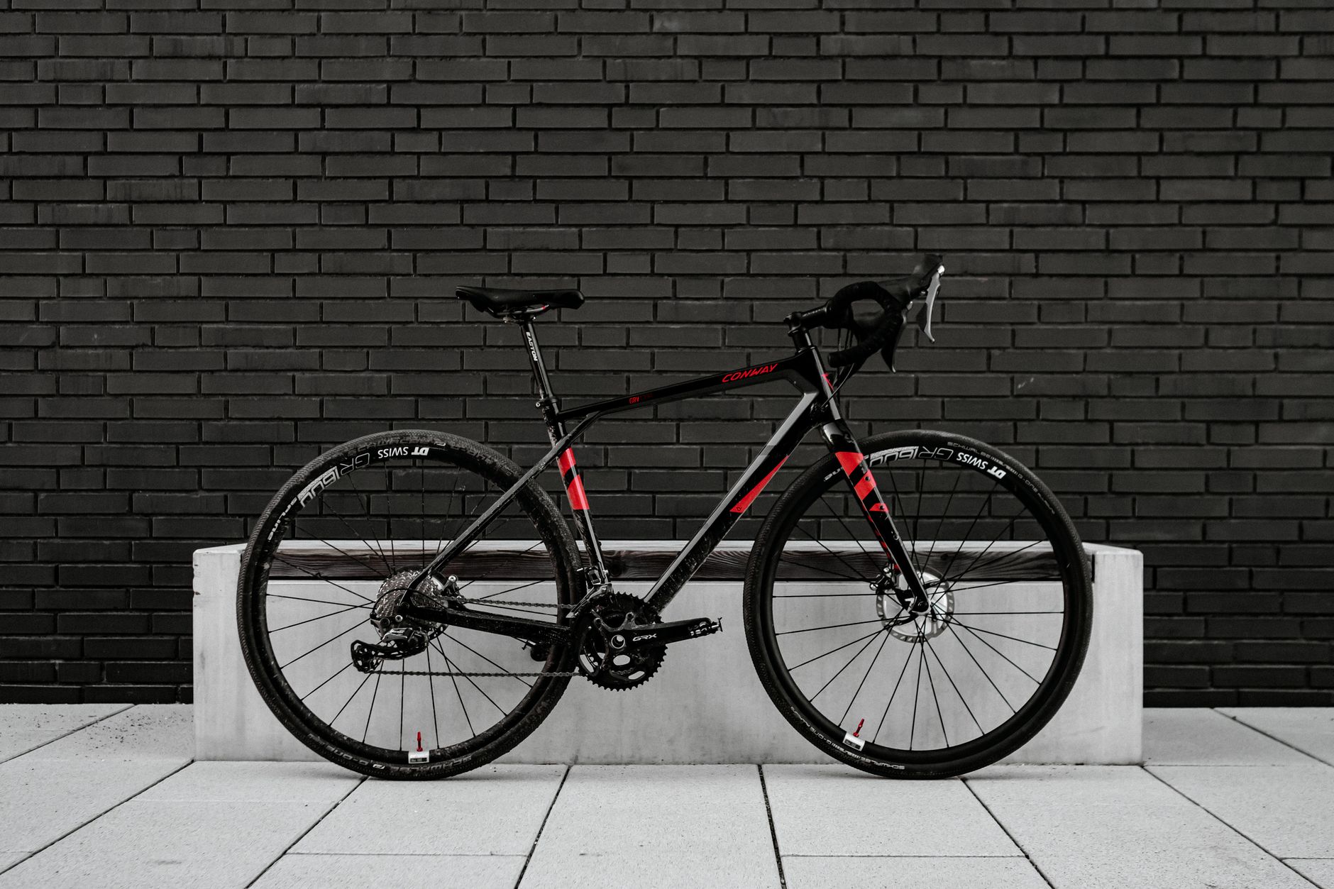 Sleek black and red road bike leaning on a modern brick wall.