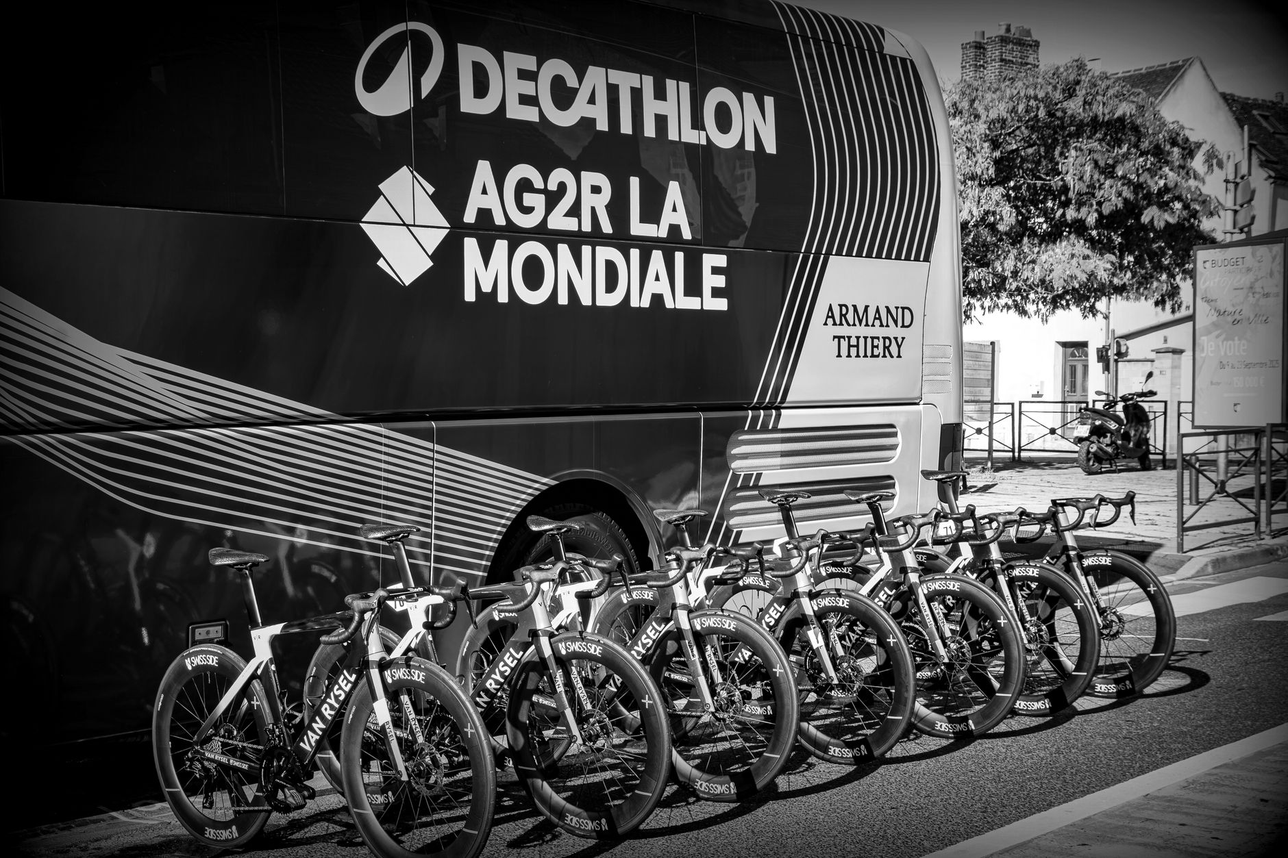 Row of professional racing bicycles lined up in front of team bus, monochrome style.