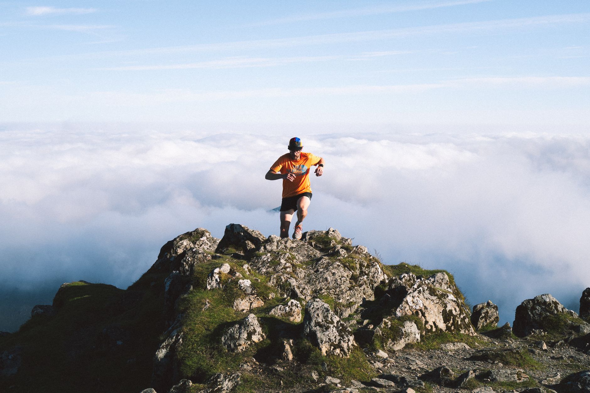Man running on rocky mountain peak above the clouds, symbolizing achievement and adventure.