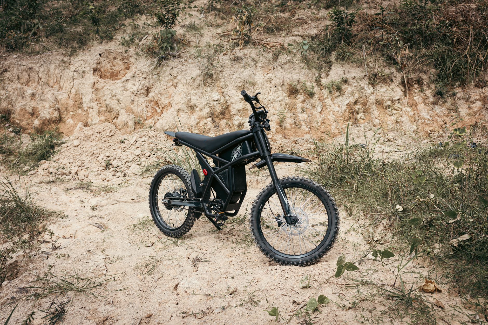 A sleek black electric dirt bike parked on a rocky outdoor trail, ready for adventure.