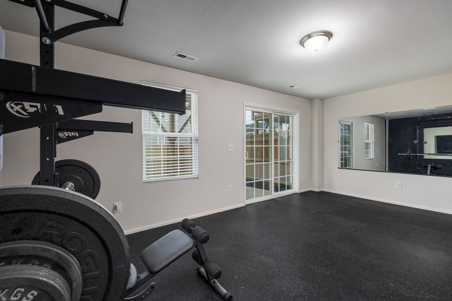 A well-lit, spacious home gym featuring modern weightlifting equipment and a large mirror.