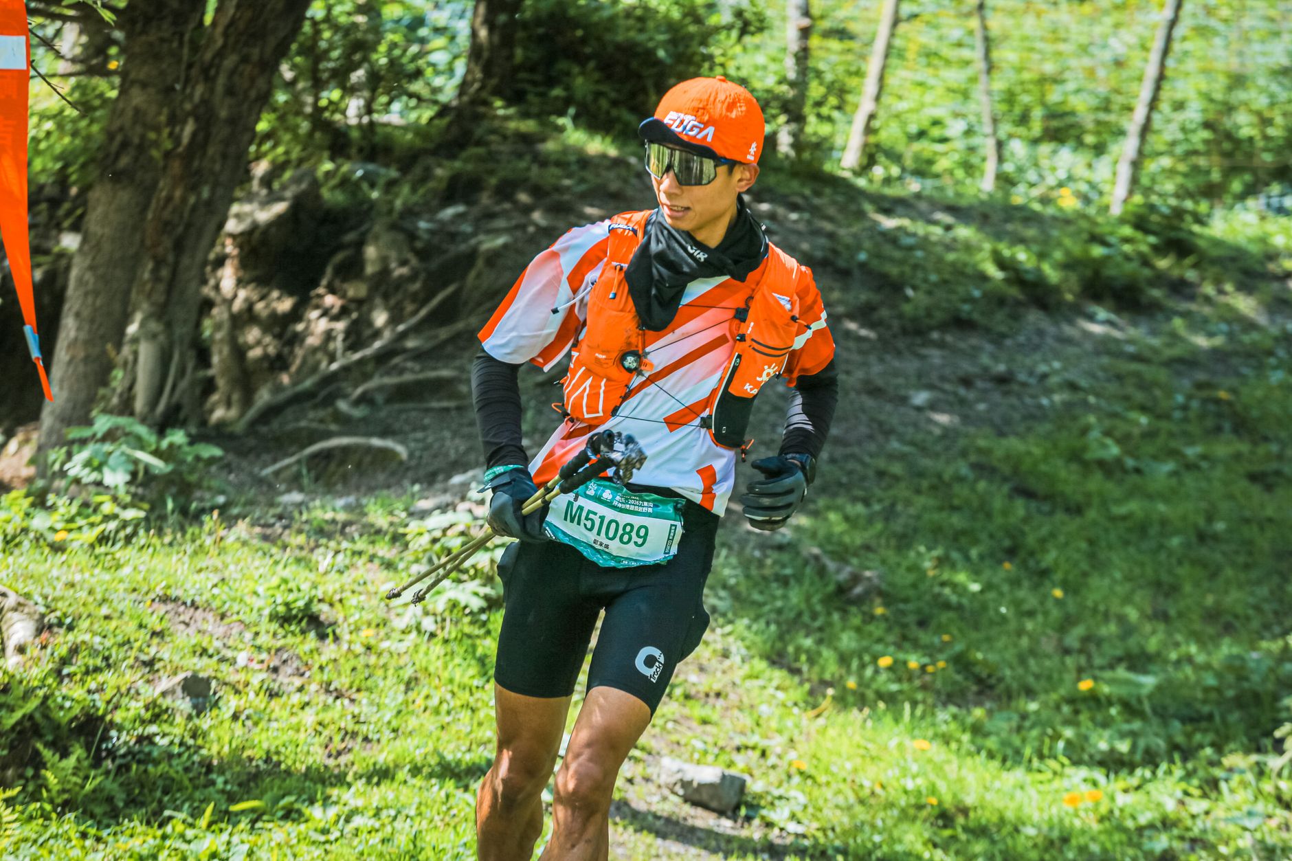 Focused trail runner in bright orange gear navigating a forest path during a race.