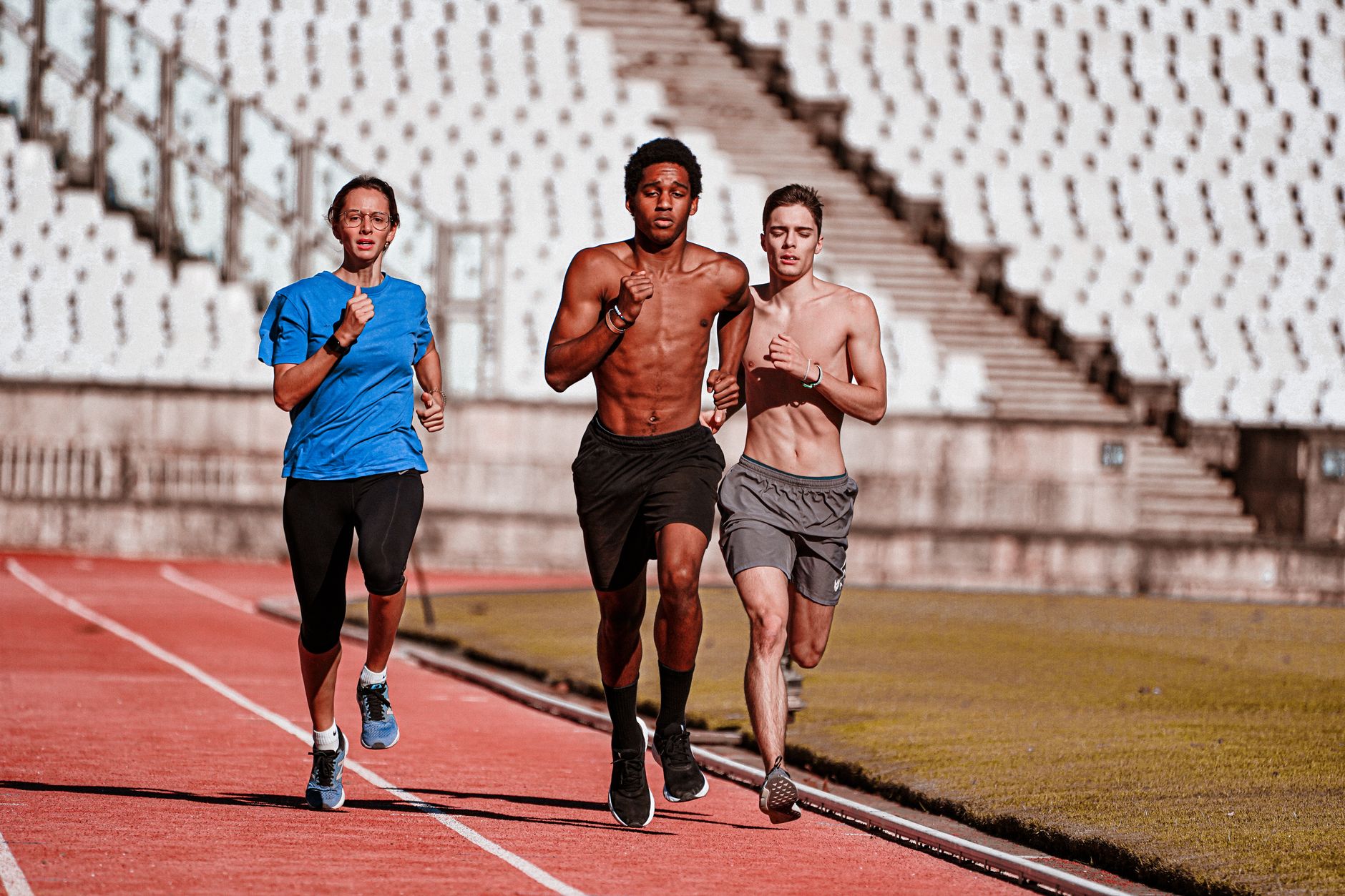 Three people running on a red track in a stadium, showcasing teamwork and physical fitness.
