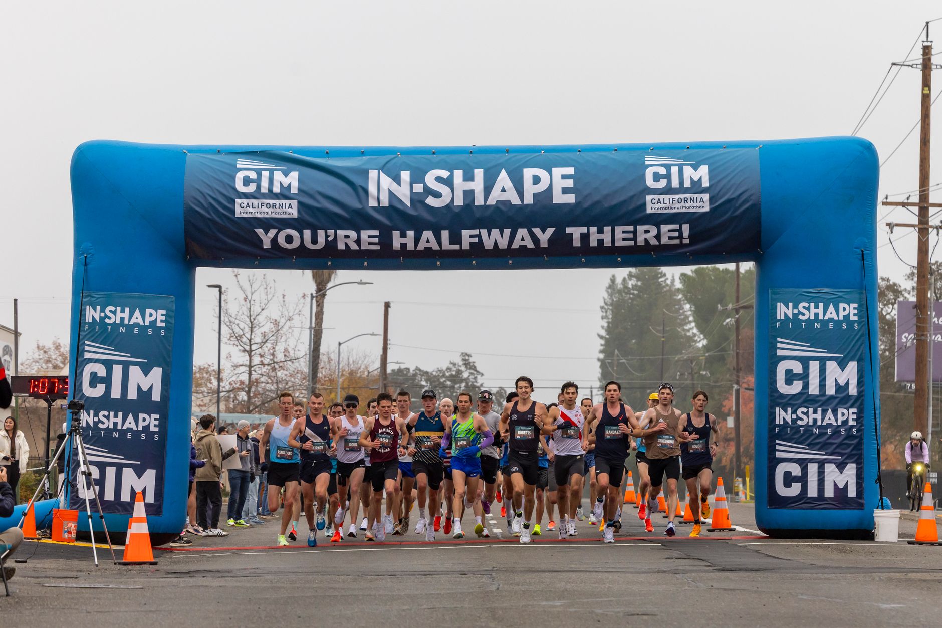 Group of runners passing halfway point in city marathon under blue inflatable arch.