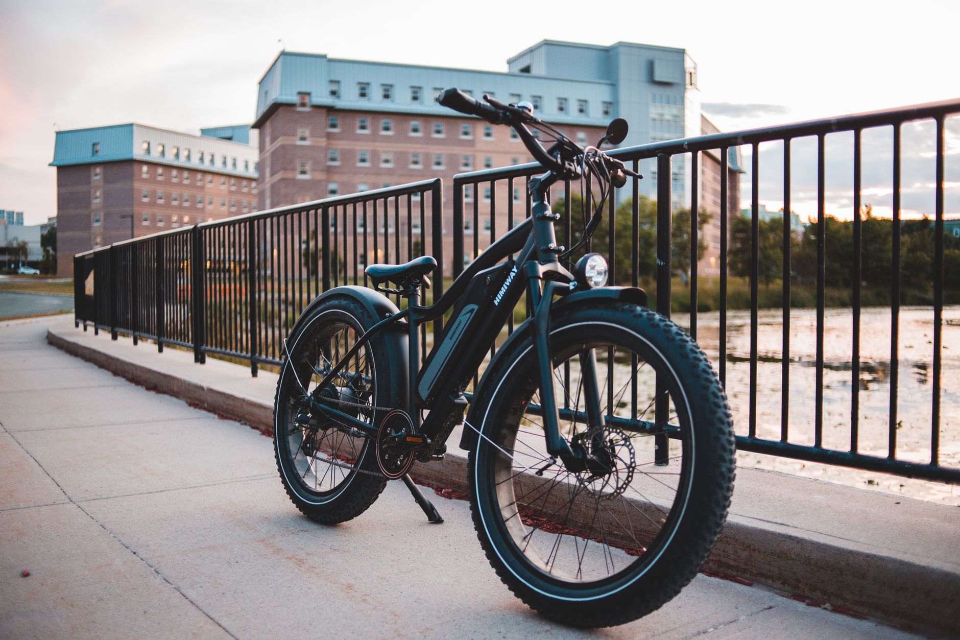 A modern electric bike parked beside a metal railing on a city sidewalk at dusk.