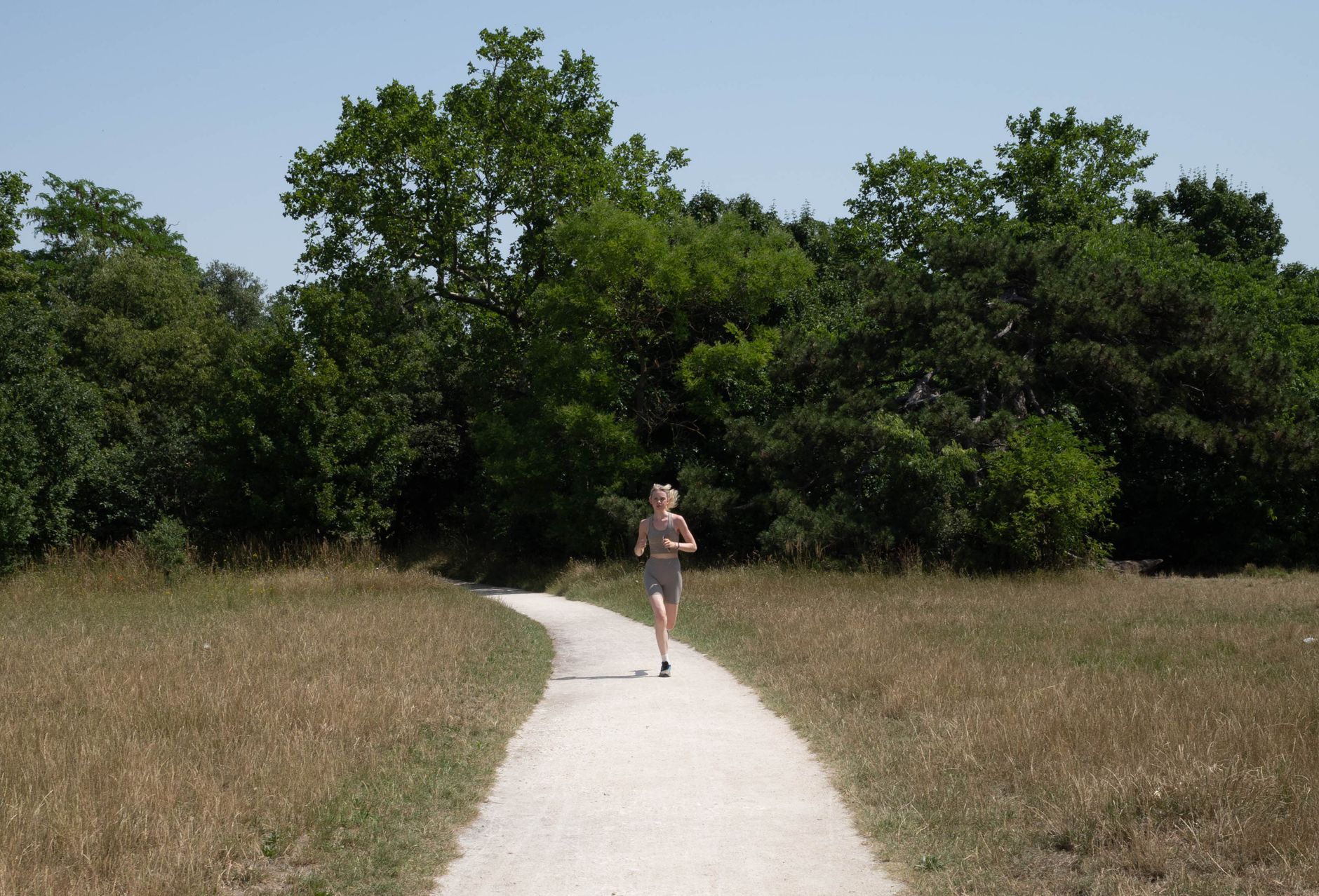 A person jogging on a sunlit forest path with lush greenery.