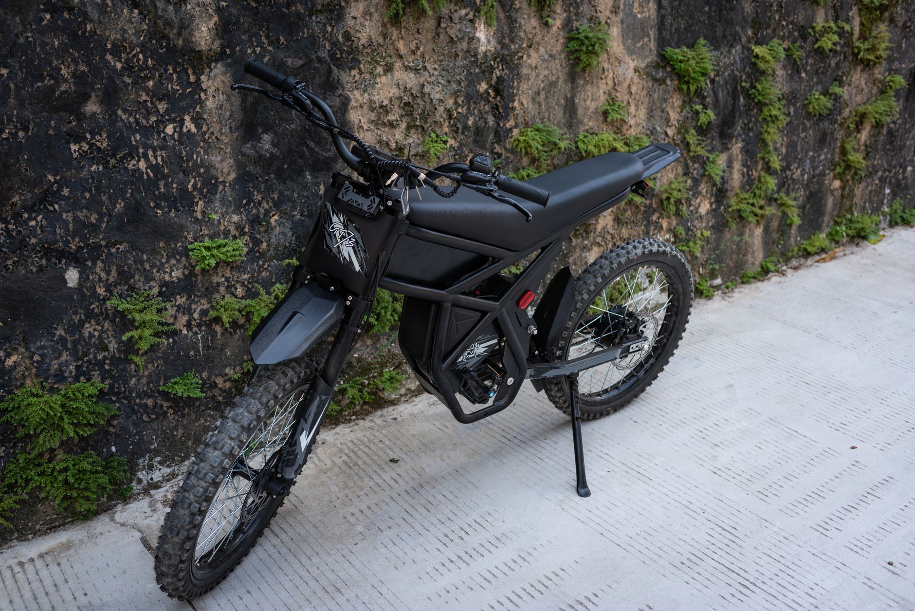 Modern black electric bike parked against a wall with green foliage on an urban street.