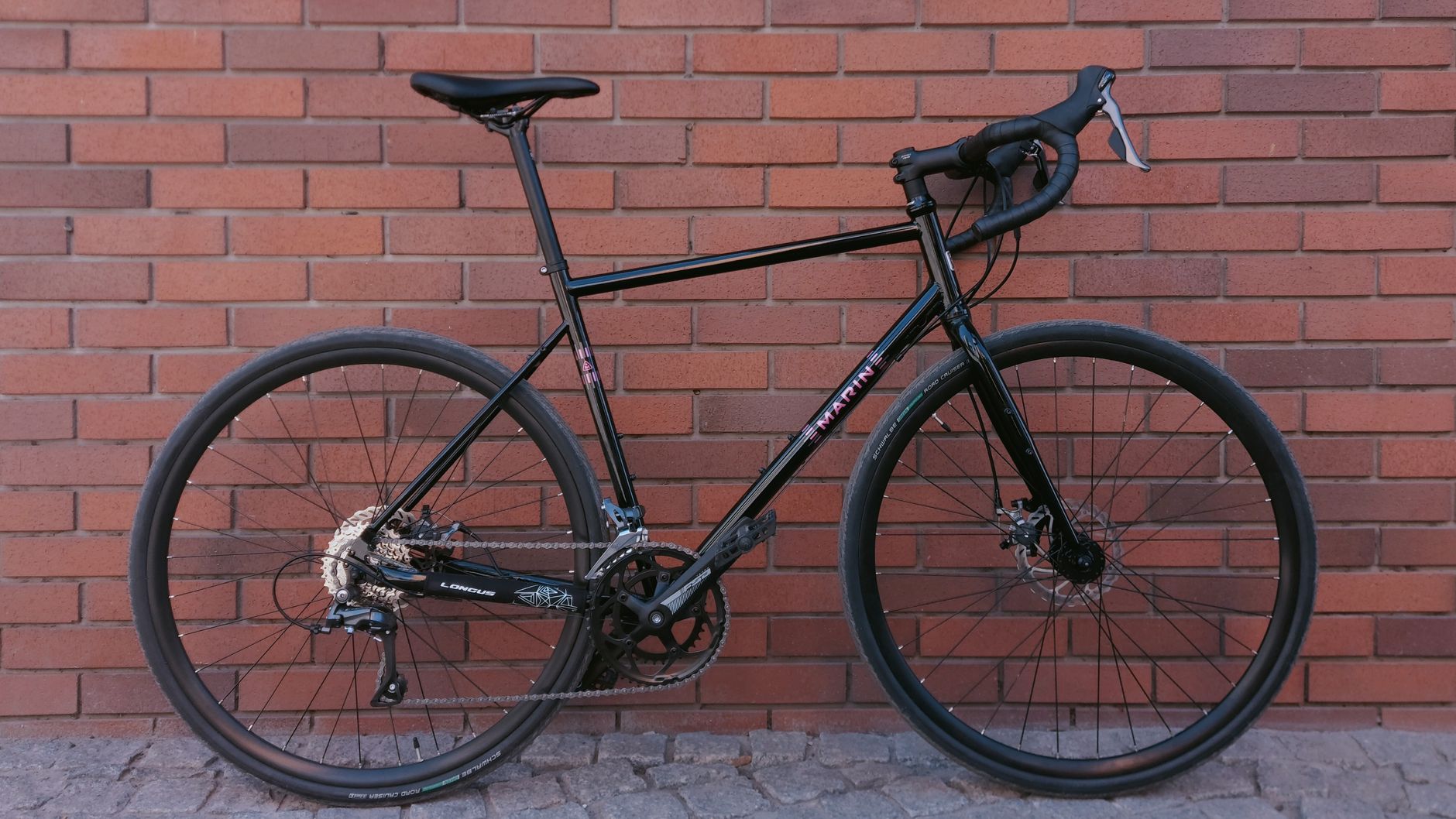 Sleek black gravel bike parked against a rustic red brick wall, perfect for urban or touring adventures.