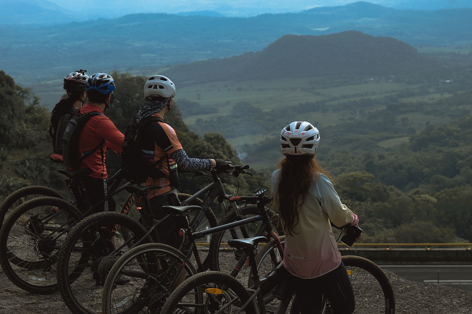 A group of cyclists stand on a hilltop enjoying a breathtaking mountain view, equipped with helmets and bikes.