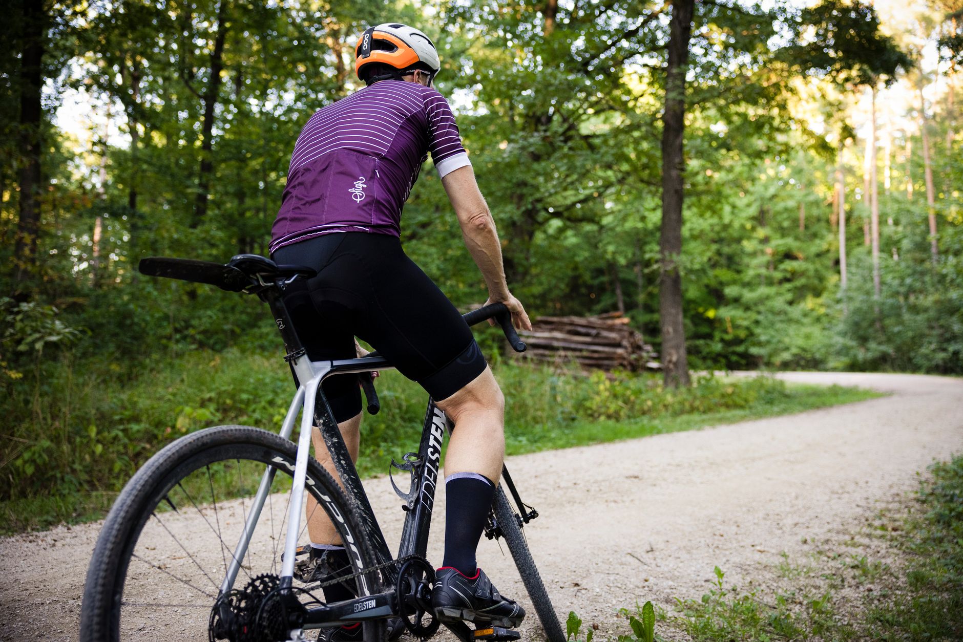 A cyclist wearing a helmet rides a road bike through a lush green forest trail.
